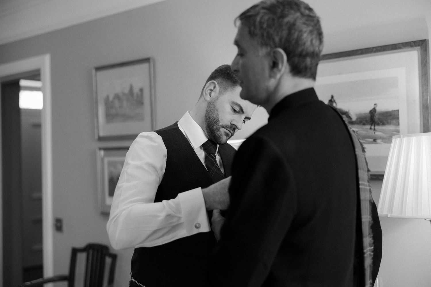 Wedding party members in formal attire gathered indoors for black and white photos.