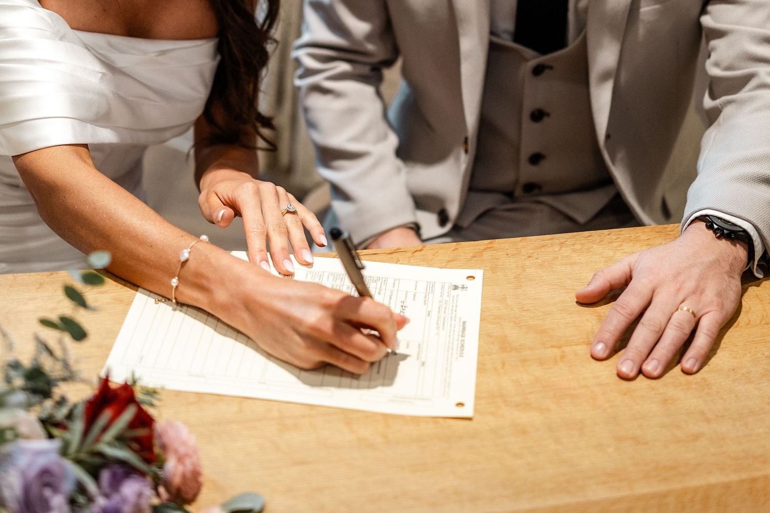 Close-up shots of hands signing wedding documents on a wooden table.
