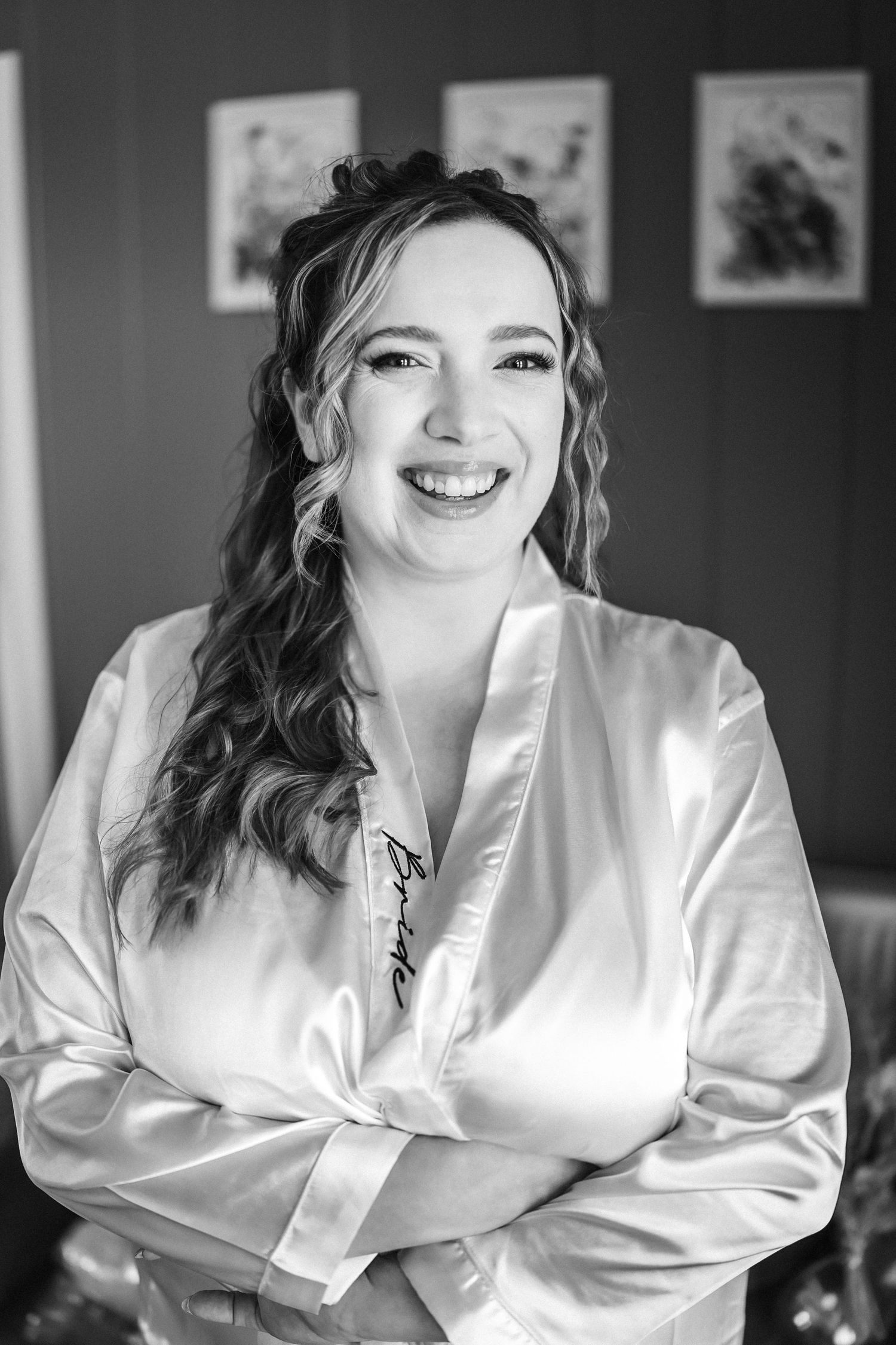 Smiling bride in satin bridal robe with curled hair poses in black and white wedding preparation photo.