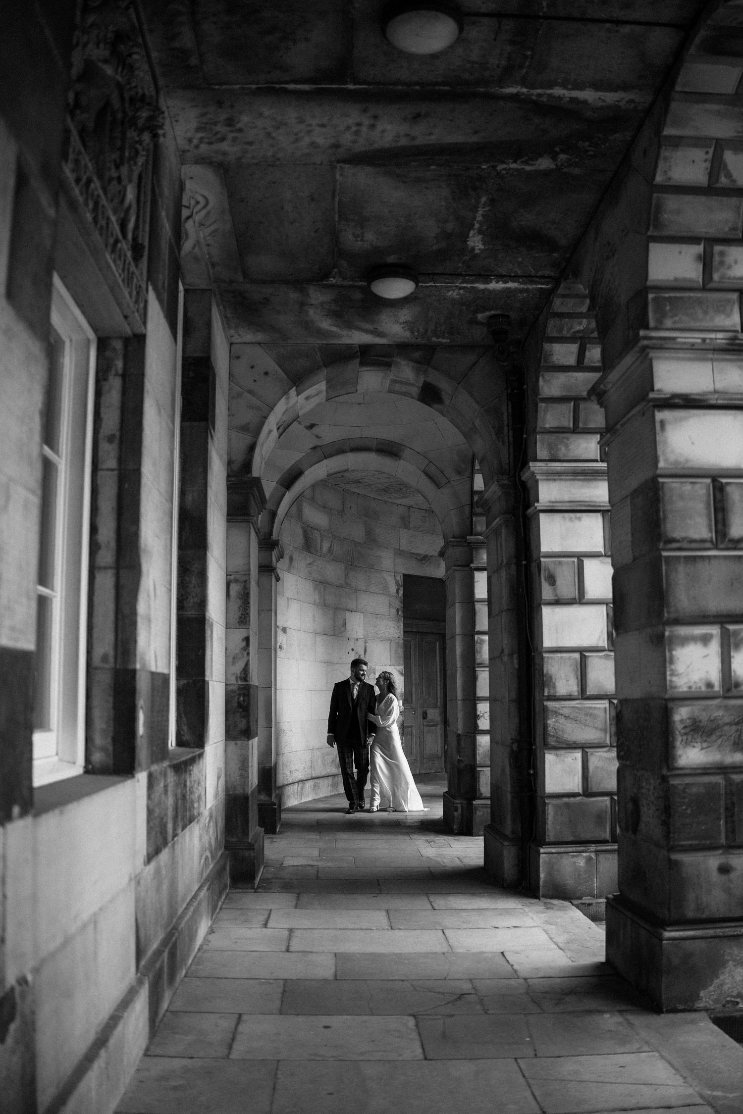 Black and white photo of bride and groom sharing a romantic moment in a grand stone archway.