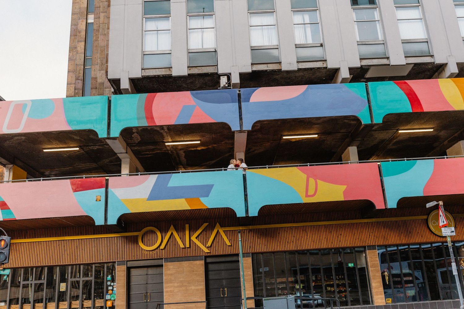Colorful geometric mural on the exterior of Oaka restaurant building with vibrant pink, blue, and red abstract street art.