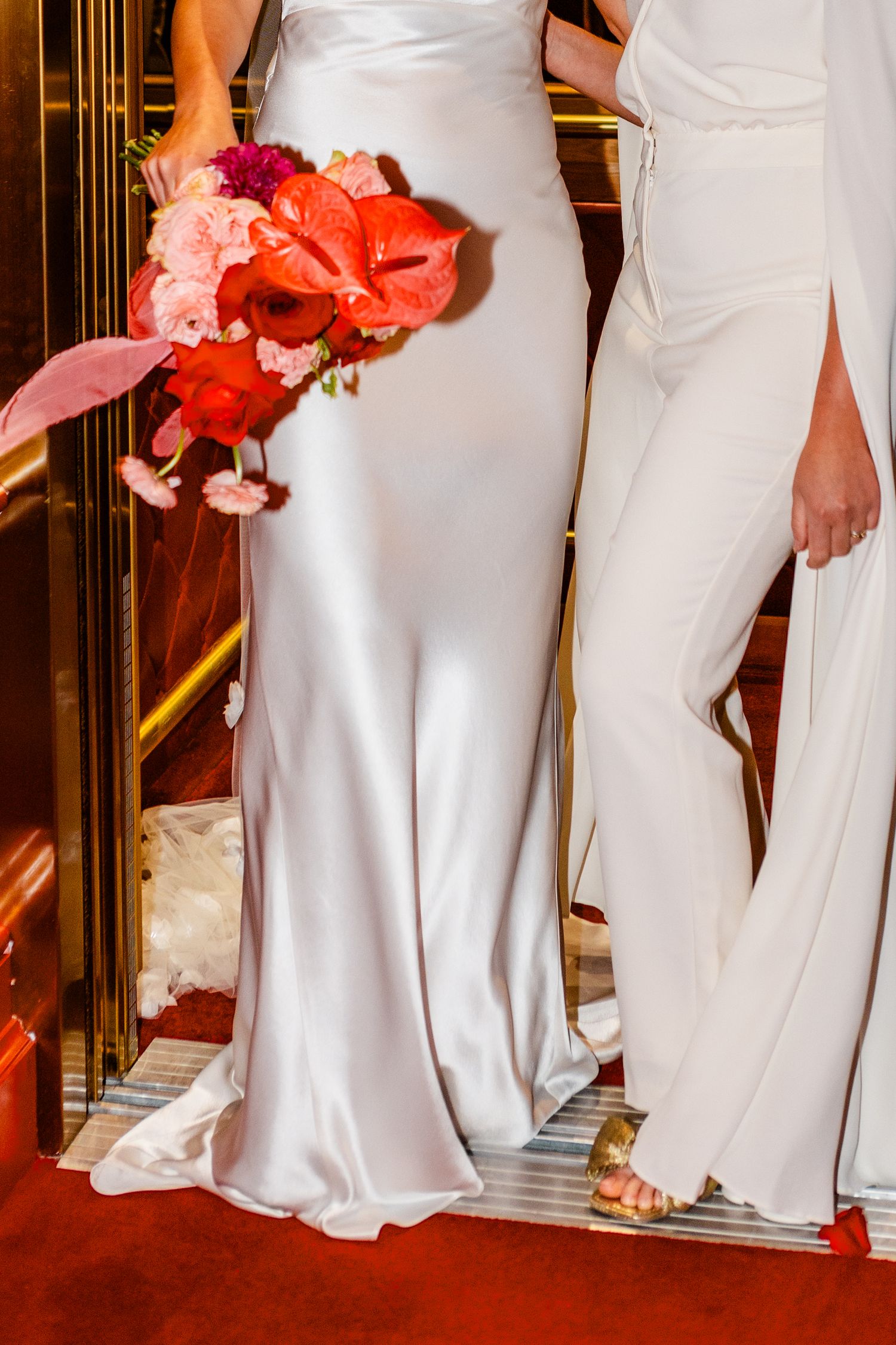 Bridesmaids in elegant white dresses stand together holding coral bouquets.