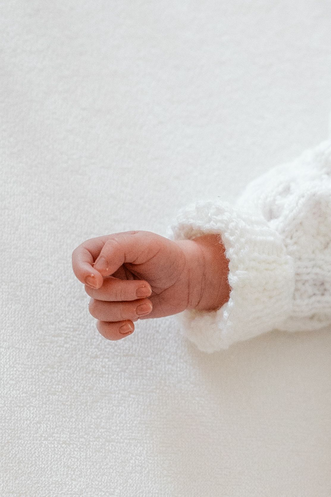 Close up of tiny baby feet wearing white knit booties against white background.