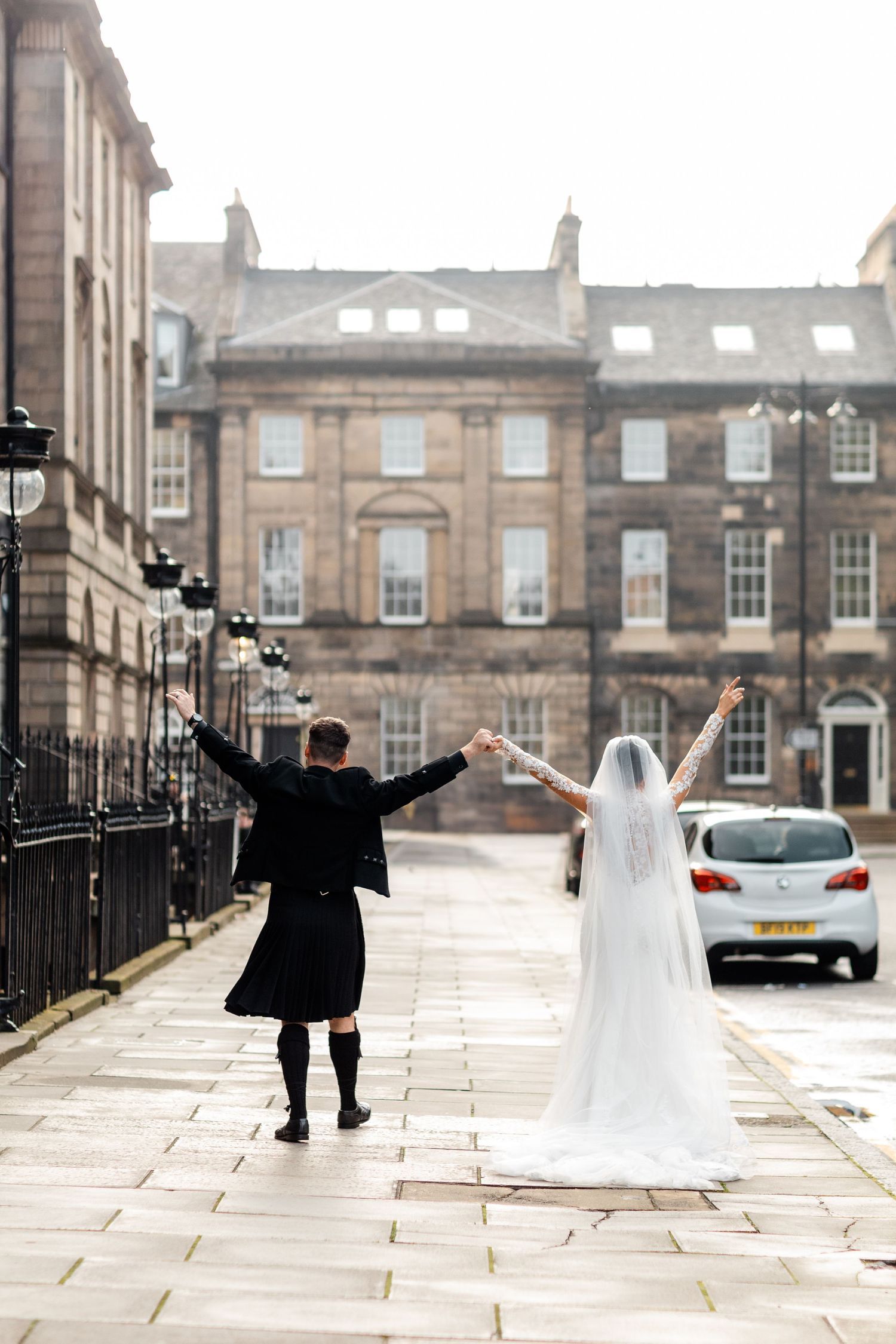 Celebratory pose of newlyweds on Edinburgh street with historic buildings in background.