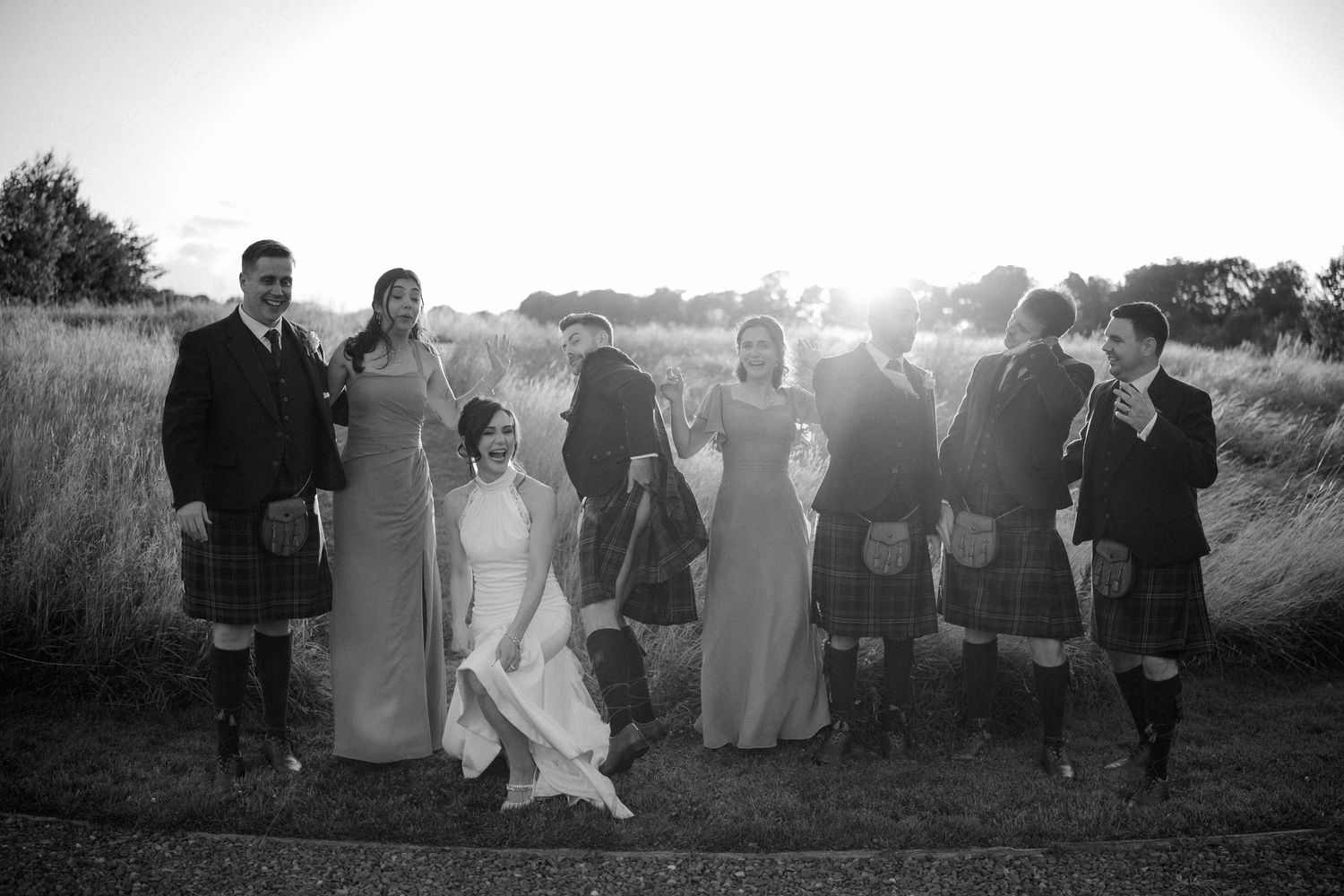 Silhouetted wedding party members standing in a field at sunset.