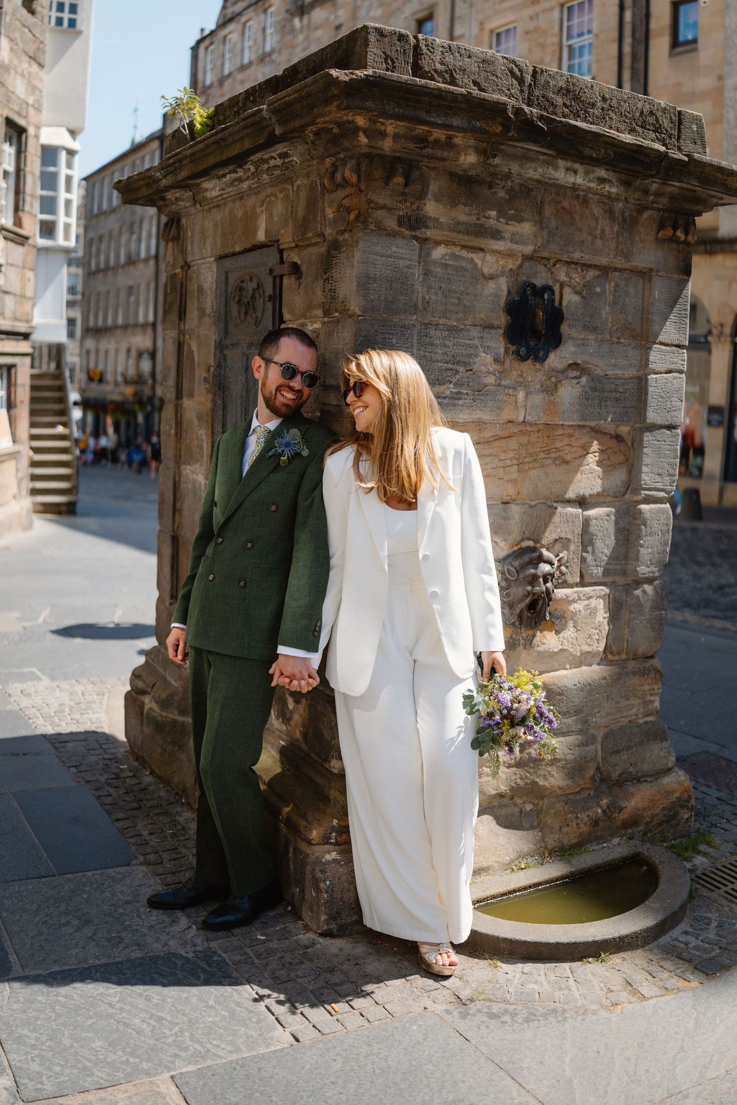 Couple posing by historic stone archway and well in Edinburgh's Old Town.