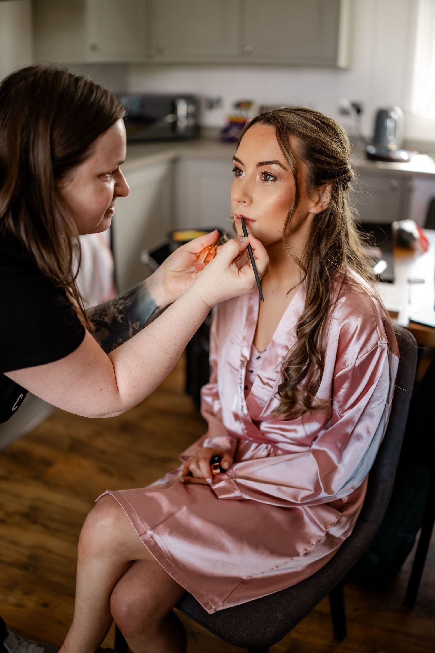 Makeup artist applies cosmetics to someone wearing a pink silk robe.