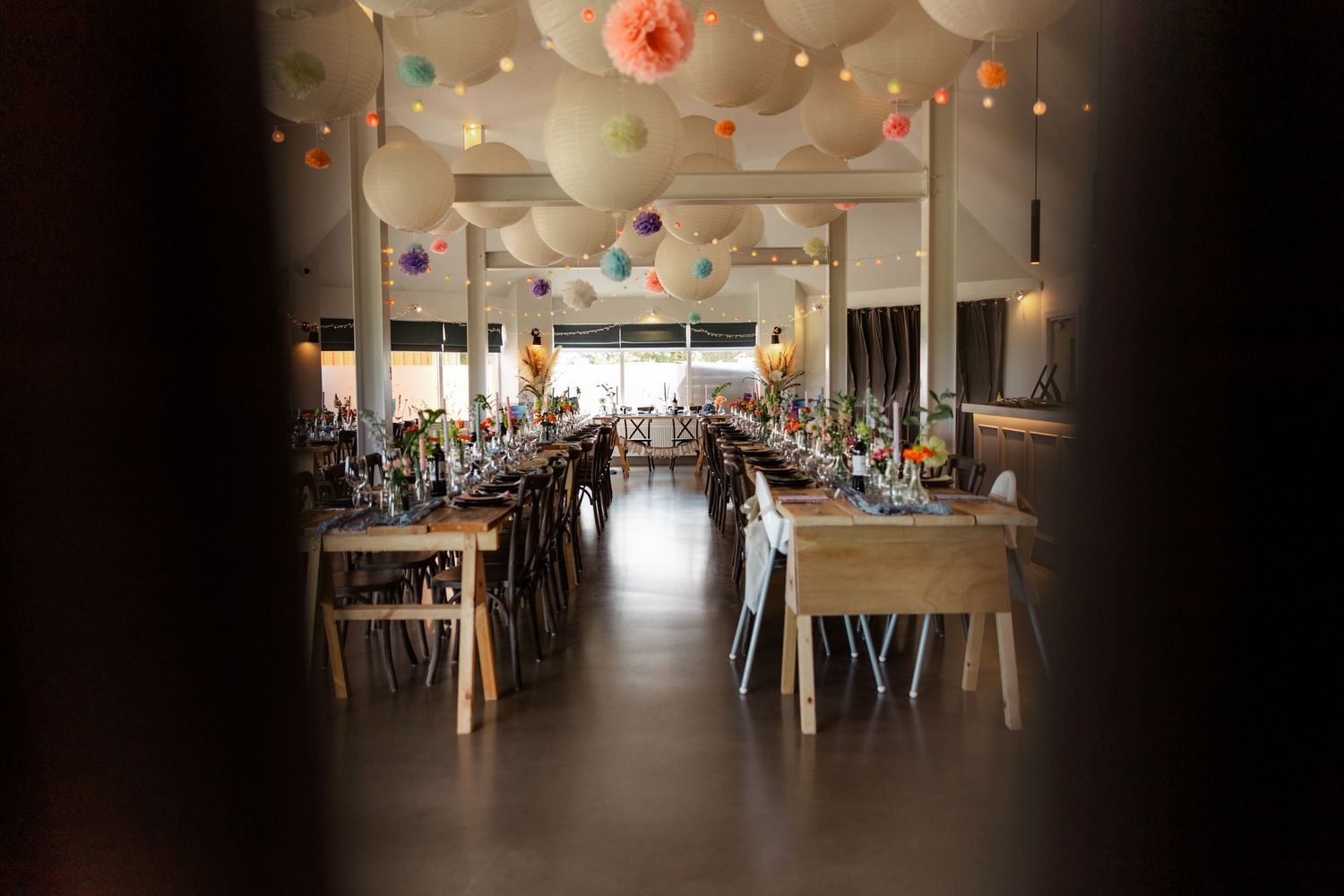 Elegant wedding reception venue with long tables and pink balloon ceiling decorations.