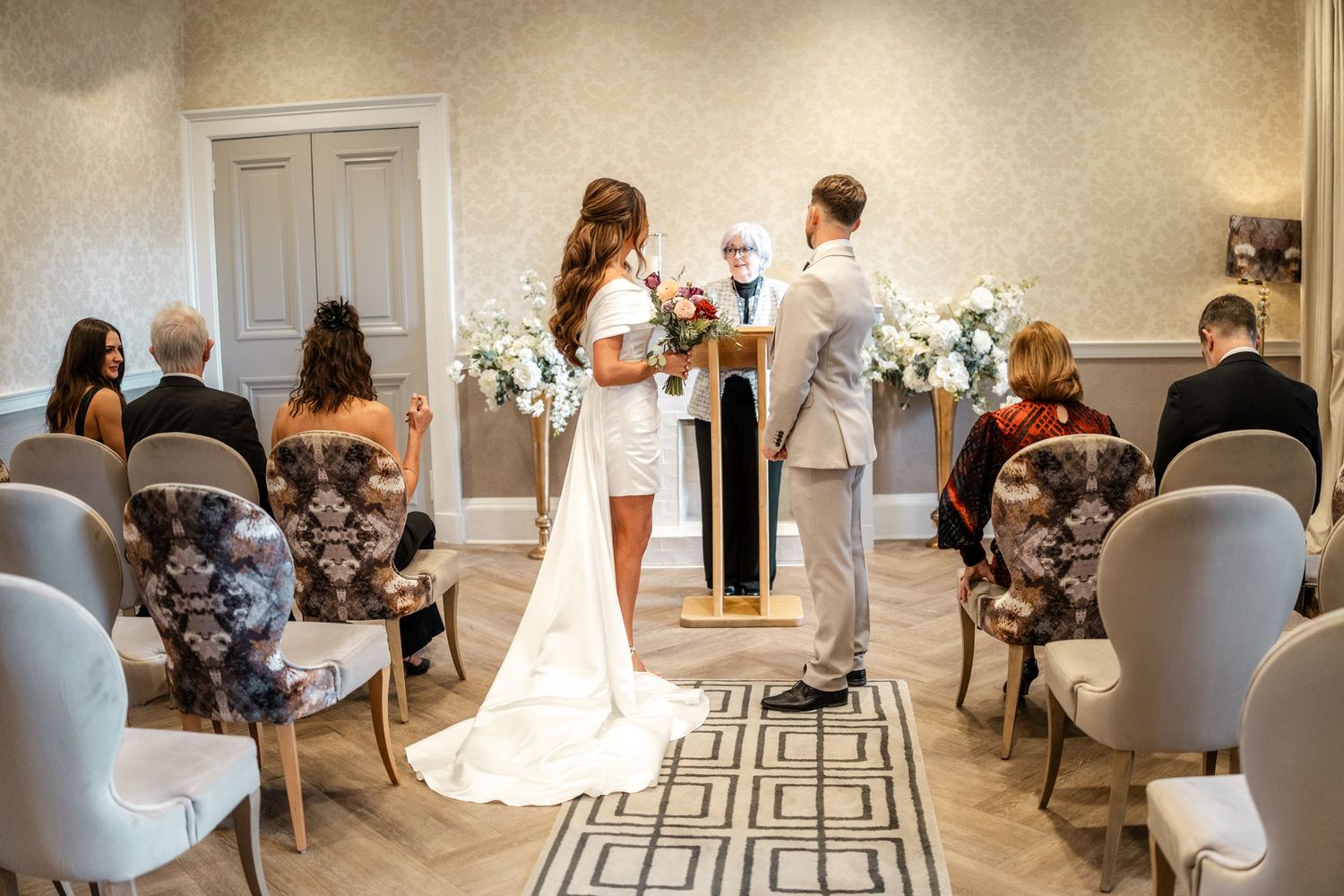 Wedding ceremony setup in bright room with white chairs and elegant decor.