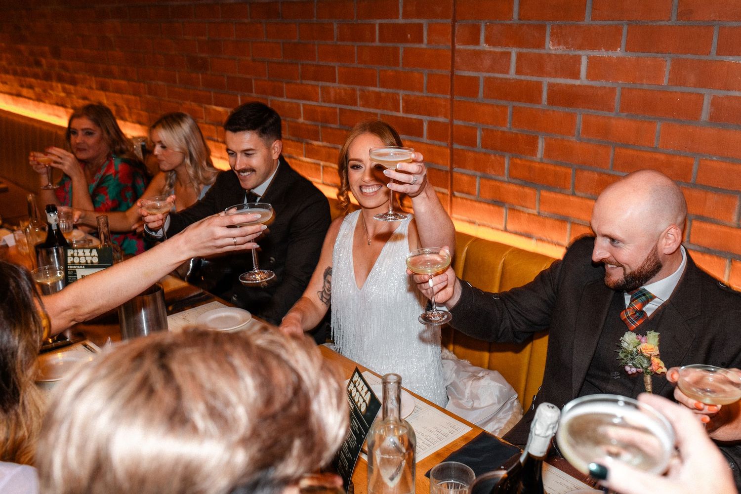 Bride and guests laughing and toasting drinks at a lively wedding reception dinner table.