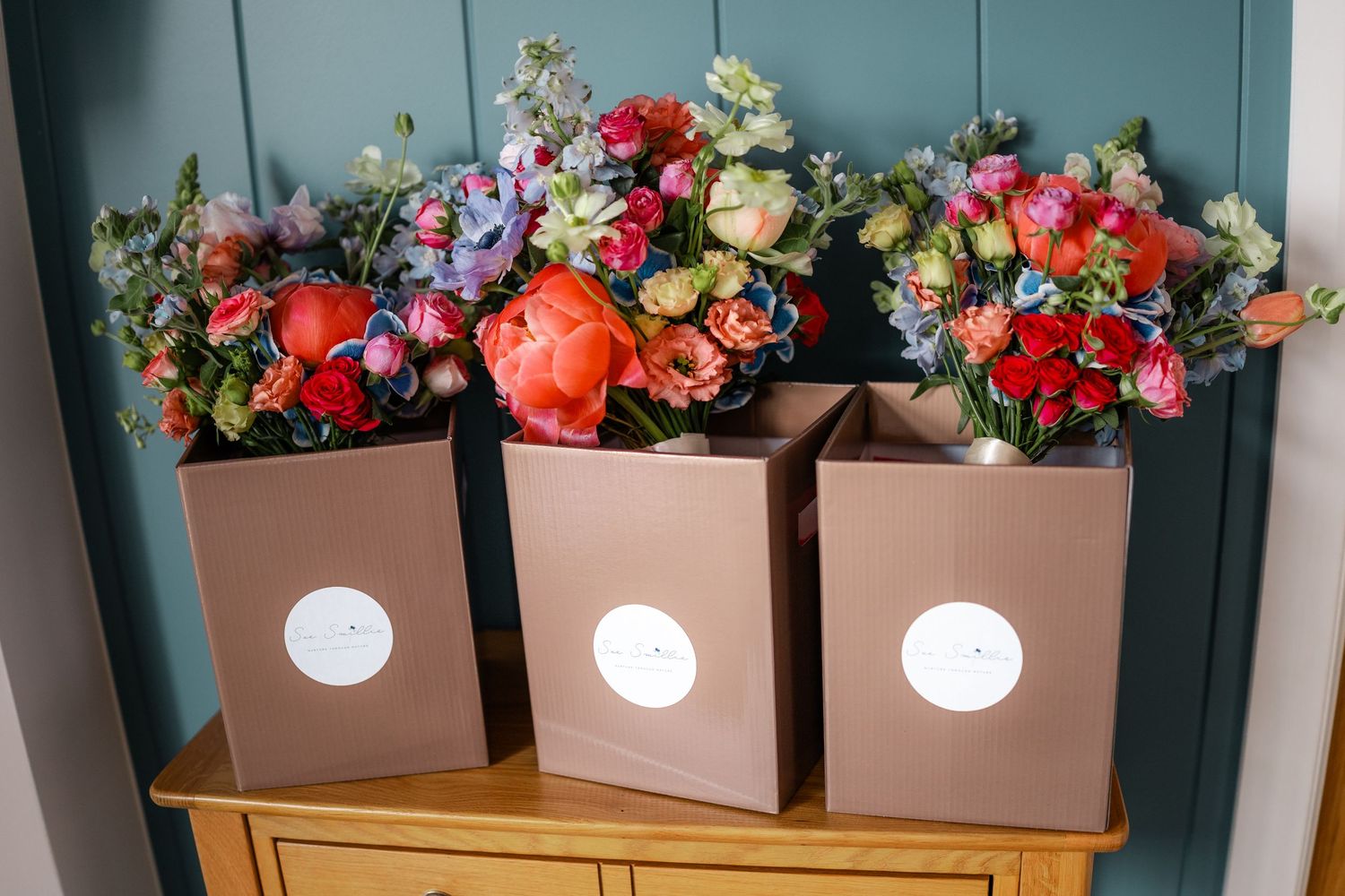 Row of wooden boxes filled with colorful fresh flowers and illuminated by hanging globe lights.