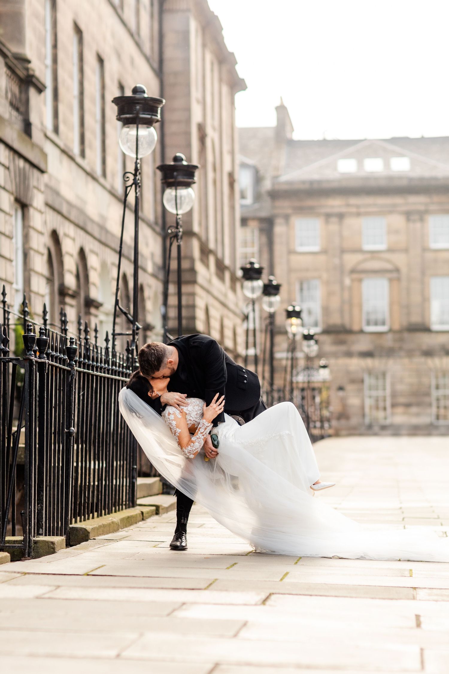 Romantic dip kiss between newlyweds on Edinburgh's historic cobblestone street.