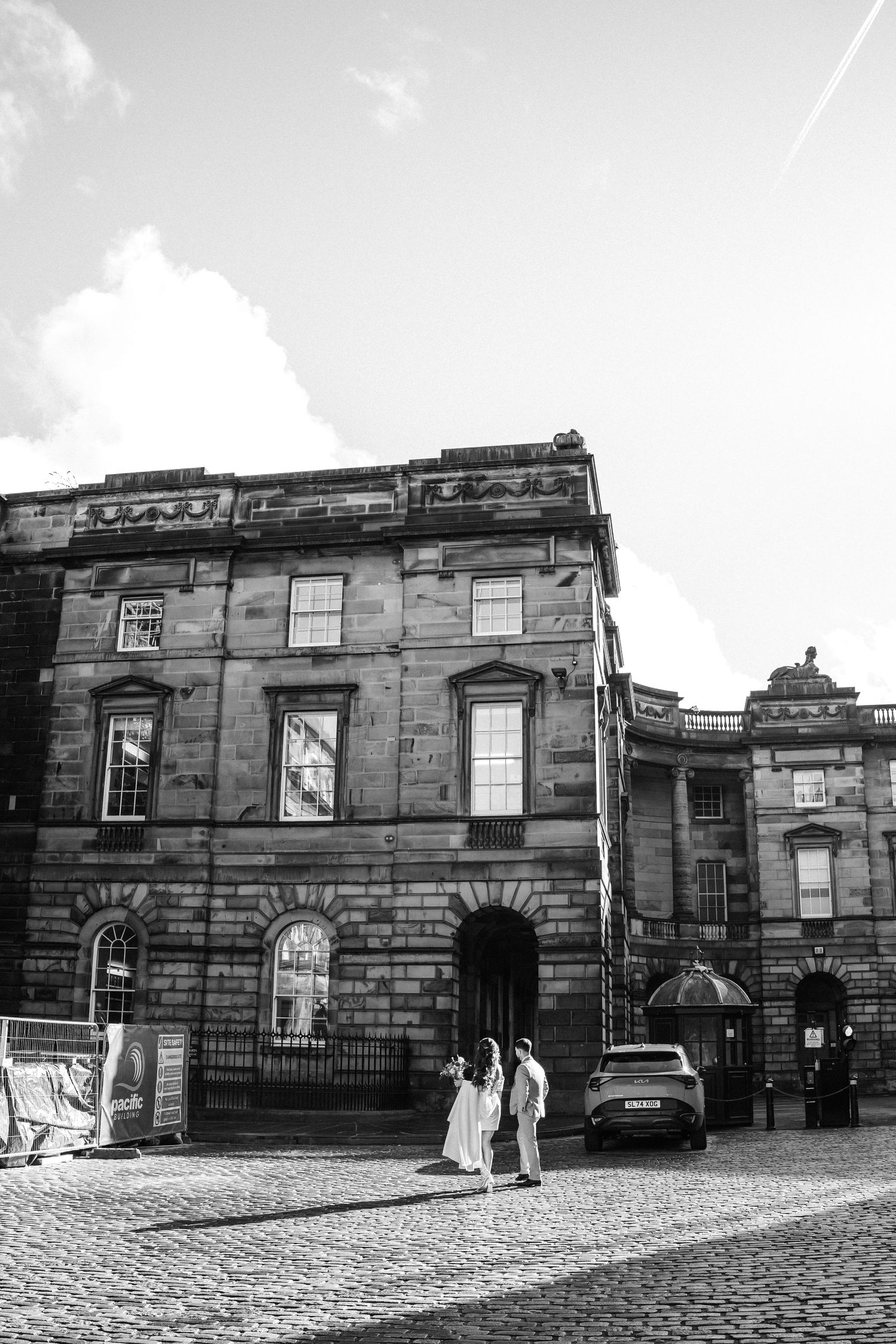 Black and white photo of a historic stone building with cobblestone street in foreground.