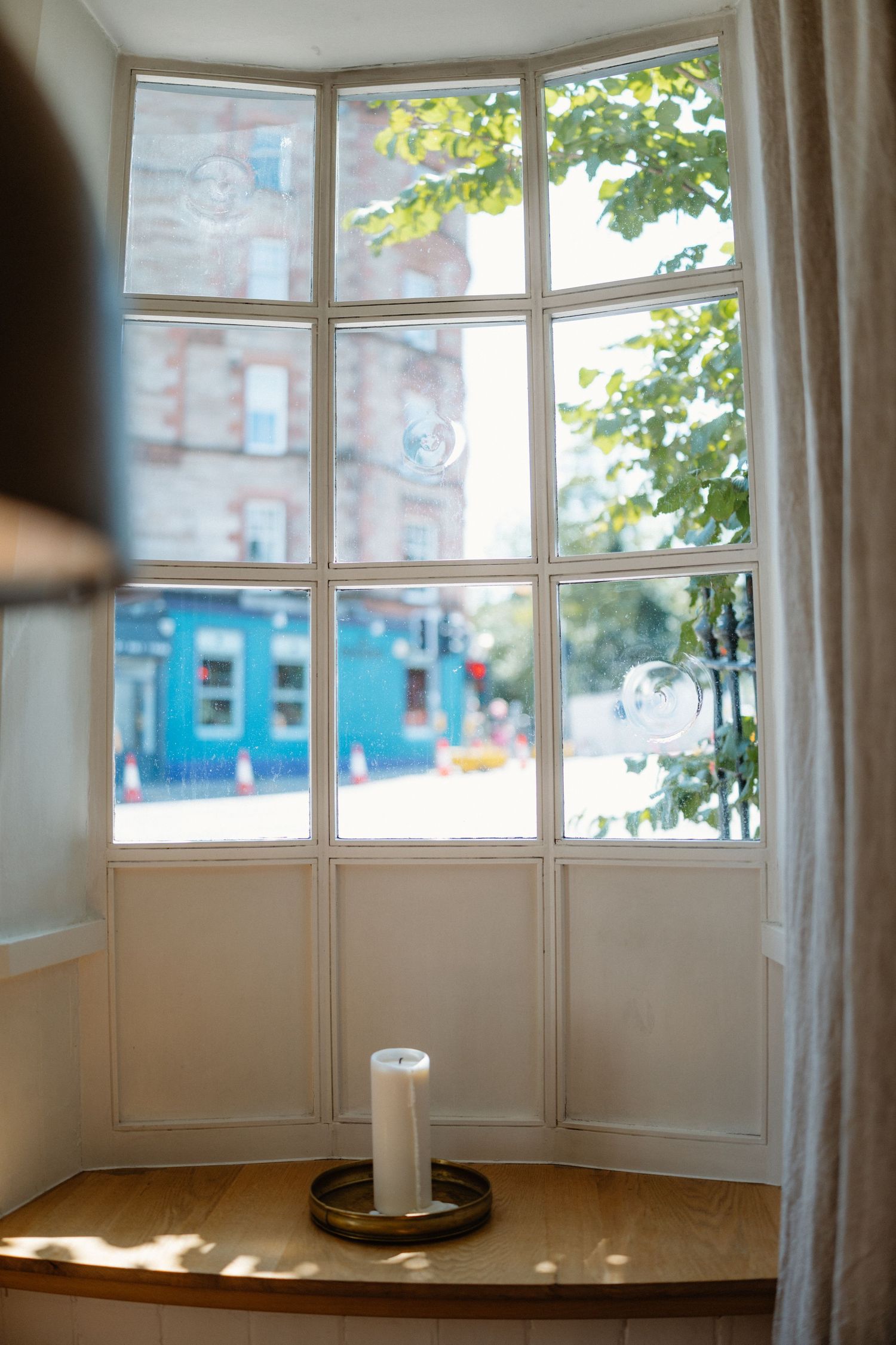 A bright bay window interior with white frames overlooking urban buildings.