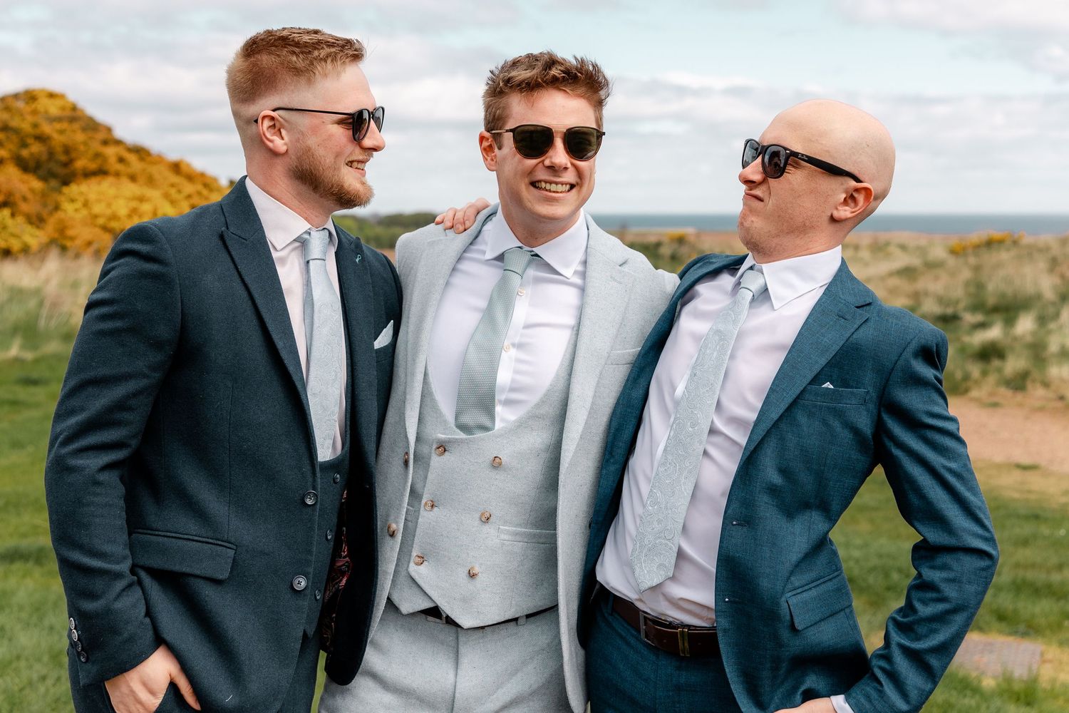 Groomsmen wearing sunglasses laugh together during outdoor wedding photos.