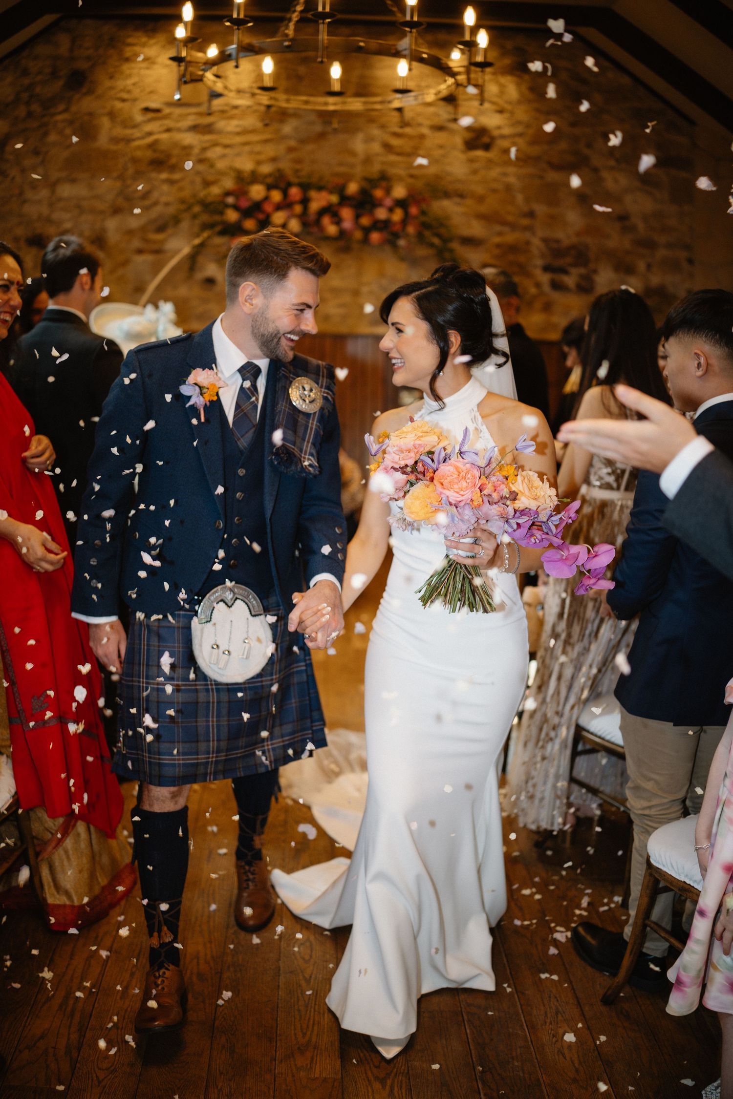 Newlyweds celebrate with confetti shower as groom wears traditional Scottish kilt.