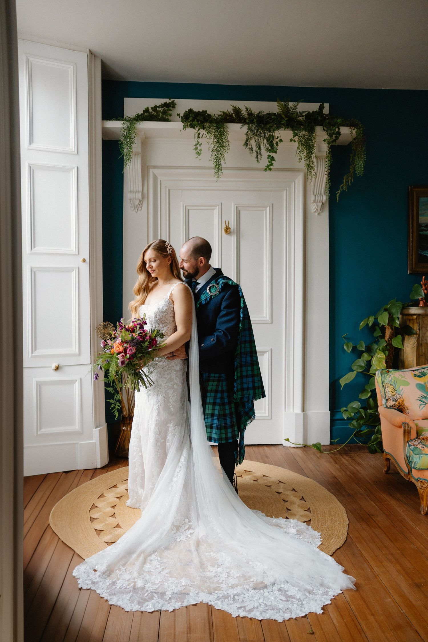 Wedding couple in elegant attire posing in room with white doors and teal walls.