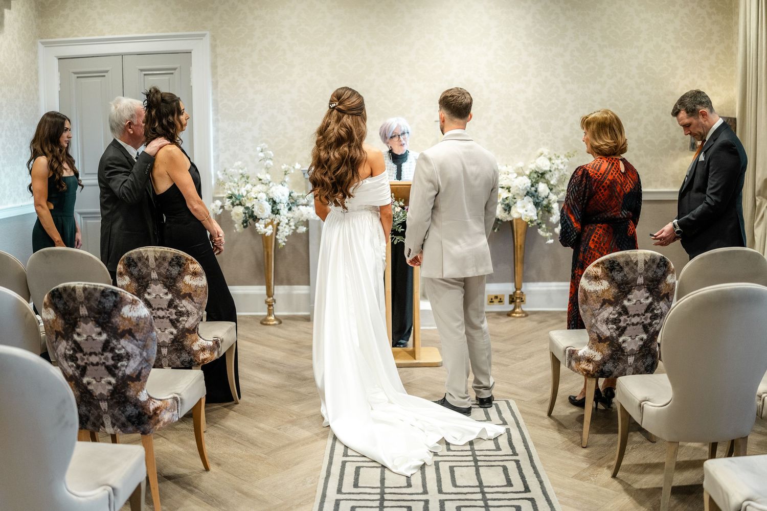 An intimate indoor wedding ceremony with elegant floral arrangements and patterned chairs in a modern venue.
