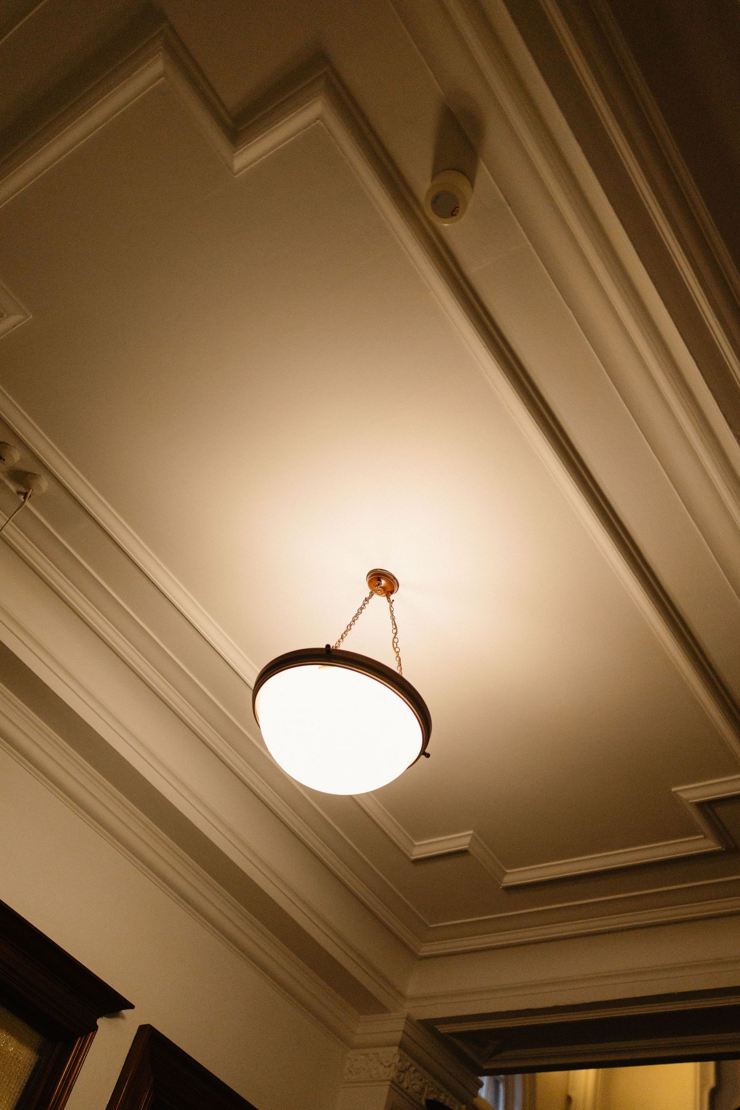 Elegant pendant light fixture hanging from ornate white ceiling molding in a classic interior.