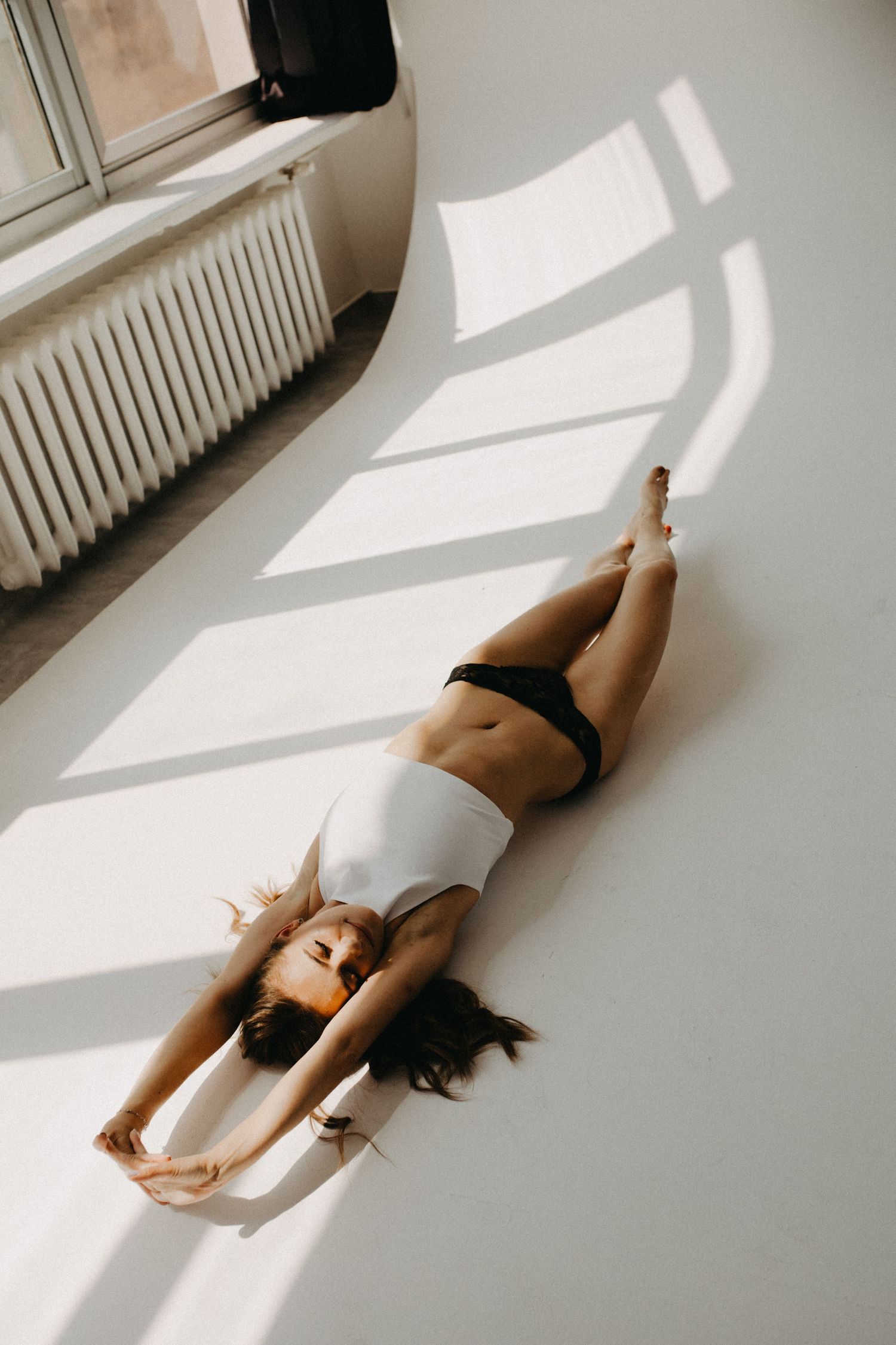 Woman in athletic wear lying on floor with dramatic window light casting geometric shadows.