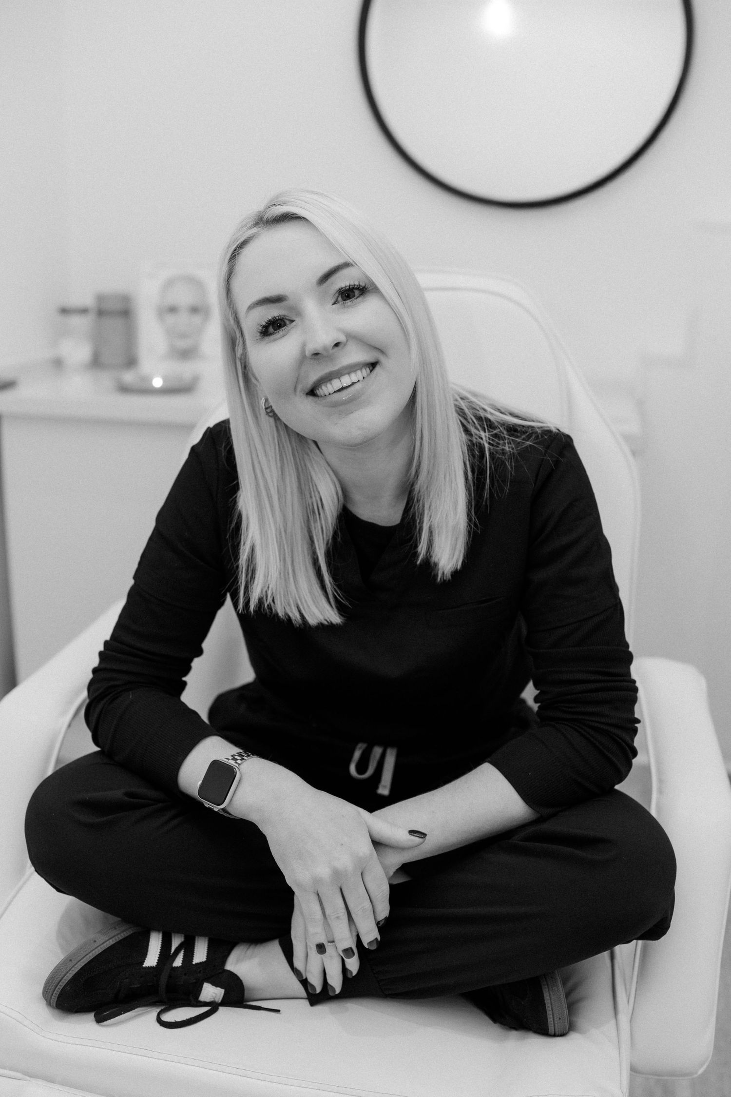 Person in black sweater relaxing on white chair in minimalist setting.