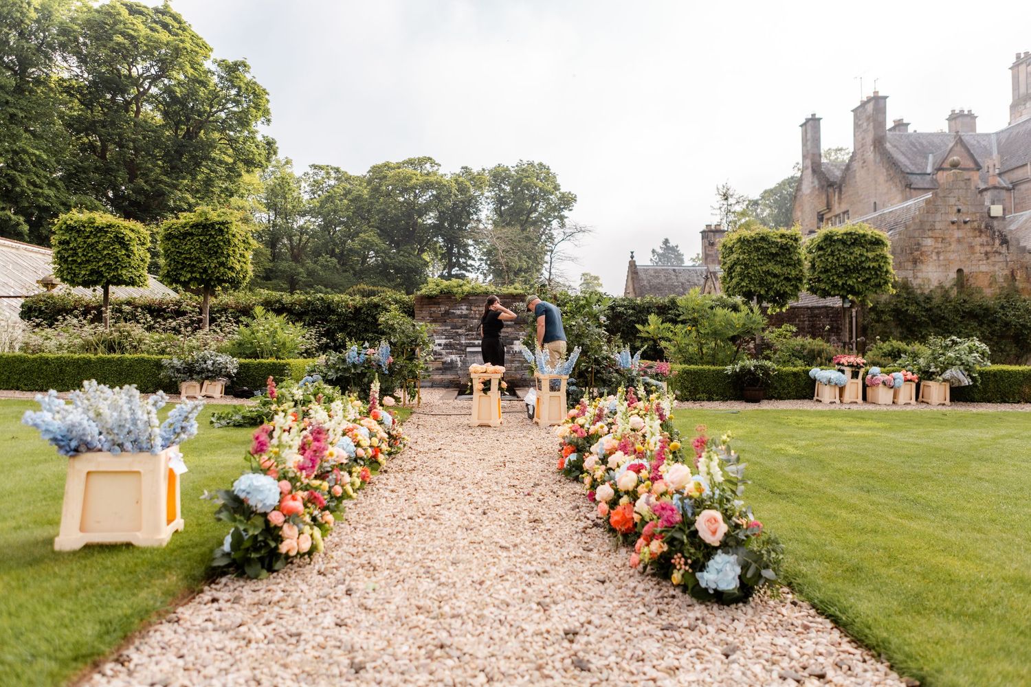 Garden pathway lined with elegant floral arrangements leading to historic building.