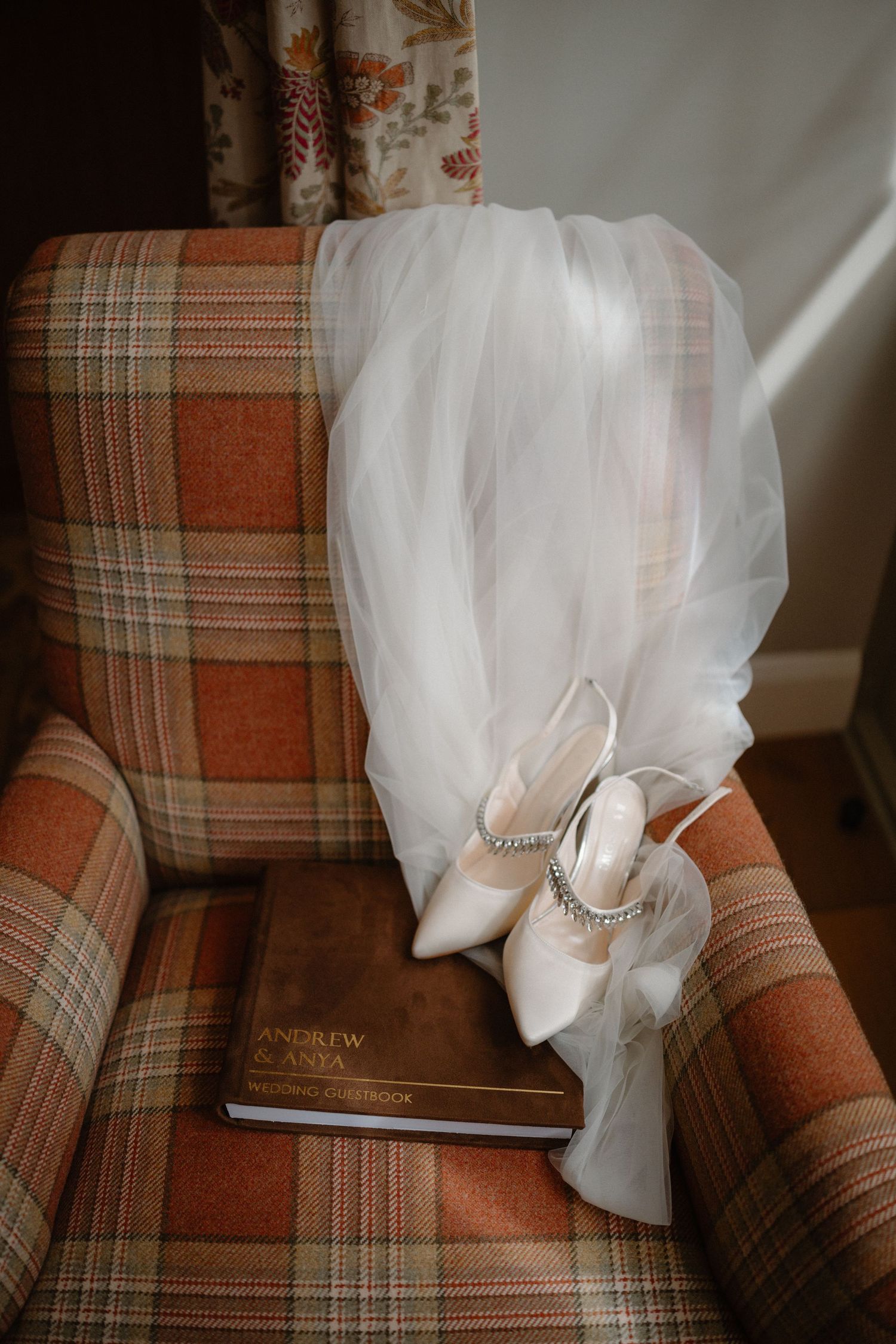 A wedding veil and book rest on a plaid orange and brown upholstered armchair in natural lighting.