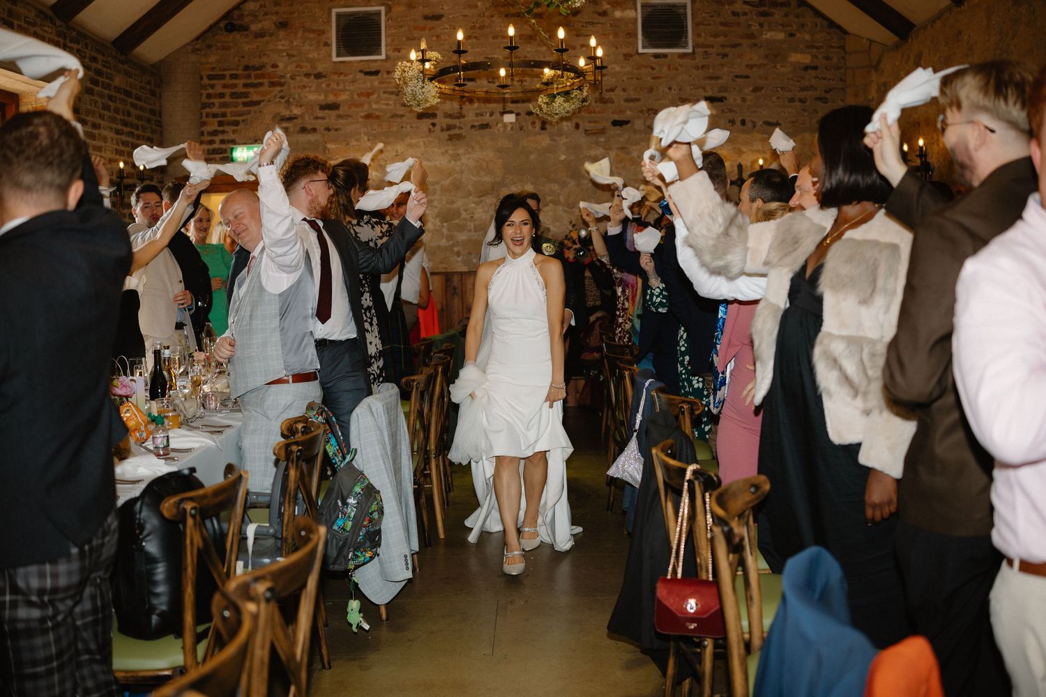 Wedding guests celebrating in rustic brick venue with exposed beams and string lights.