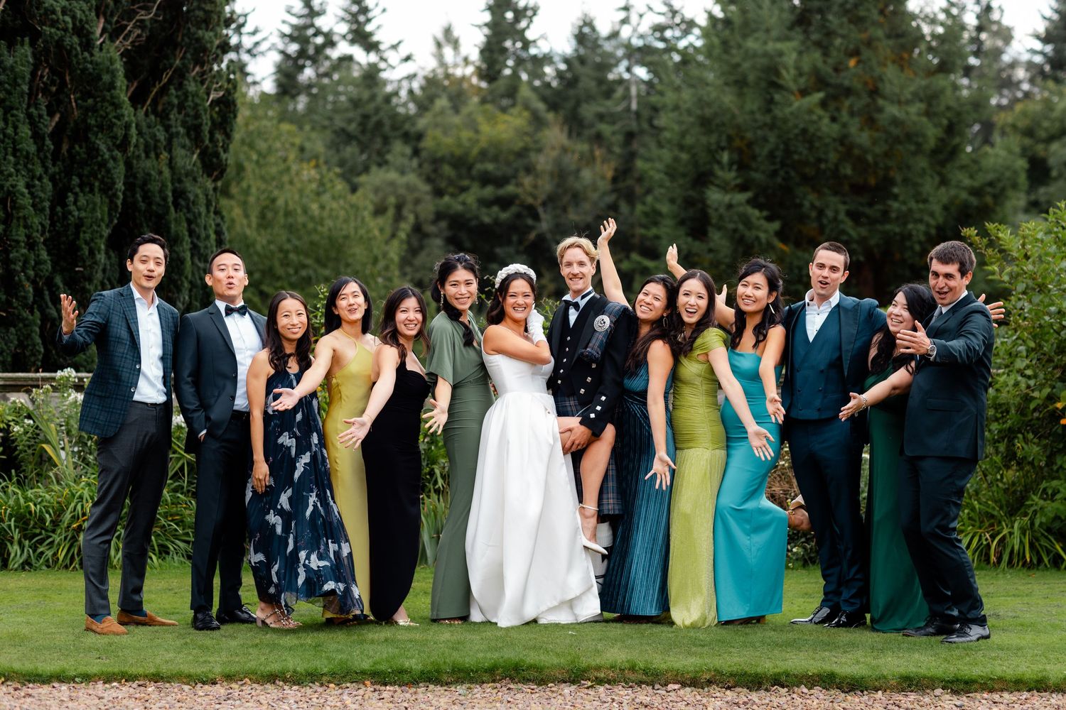 Wedding celebration group poses in mix of formal wear and colorful dresses outdoors.