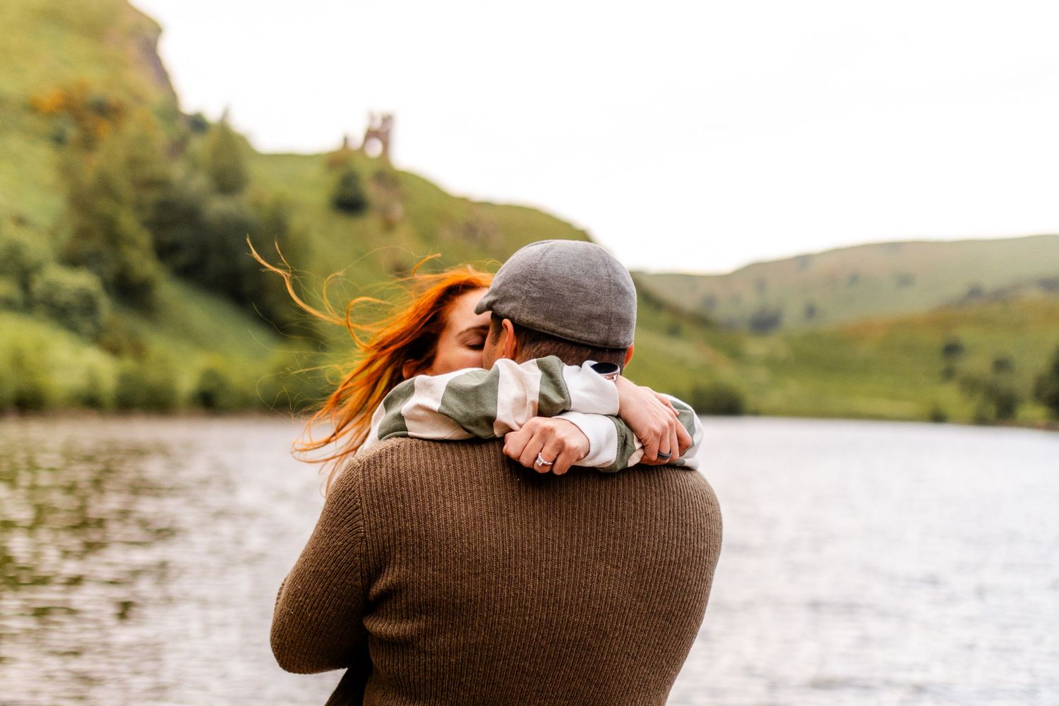 Couple embraces in front of scenic mountain lake during golden hour.