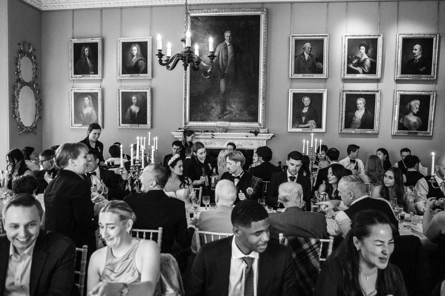Guests enjoying a formal dinner event in an elegant room with portrait-lined walls.