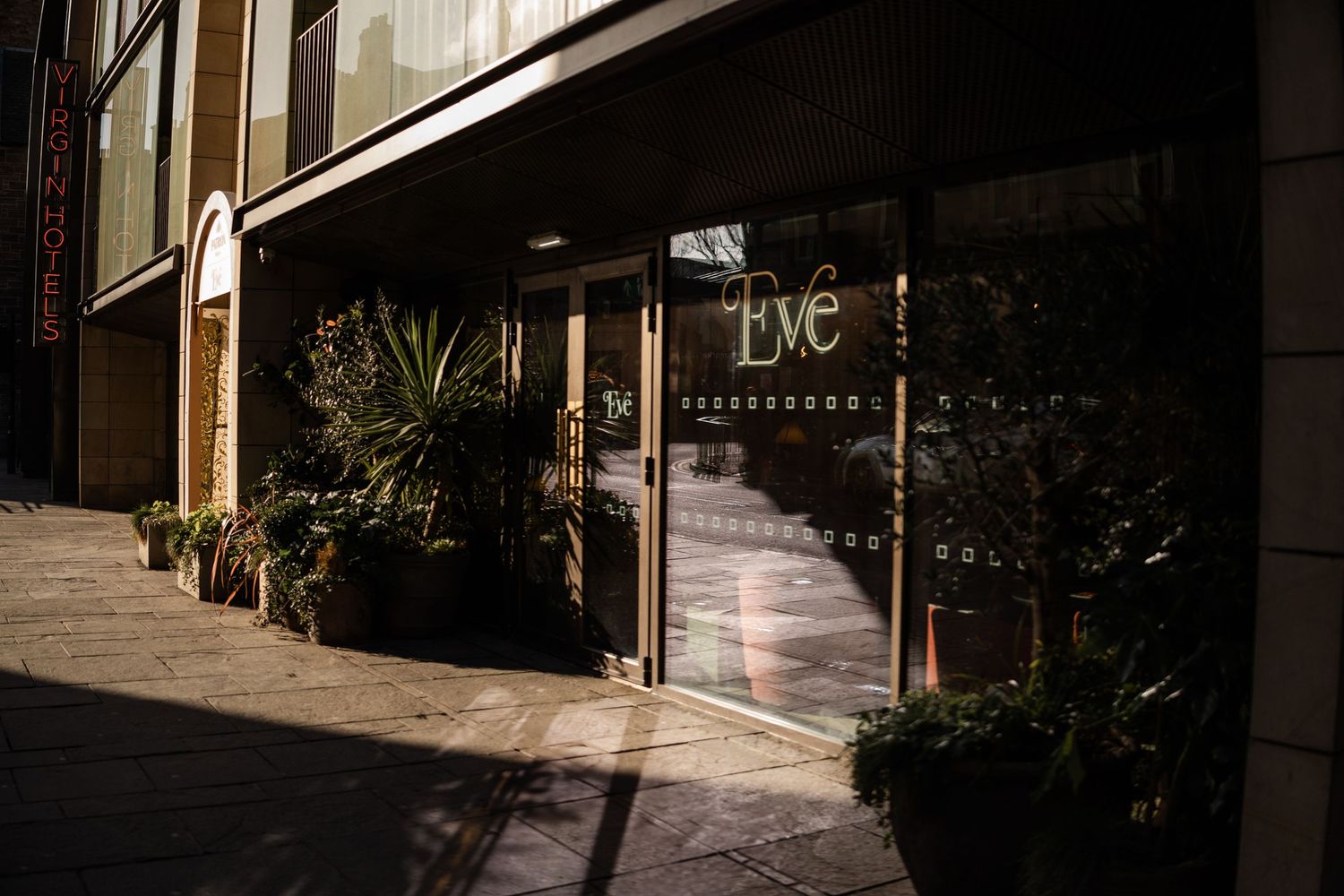 Sunlight streams through windows onto an empty urban sidewalk with storefronts.