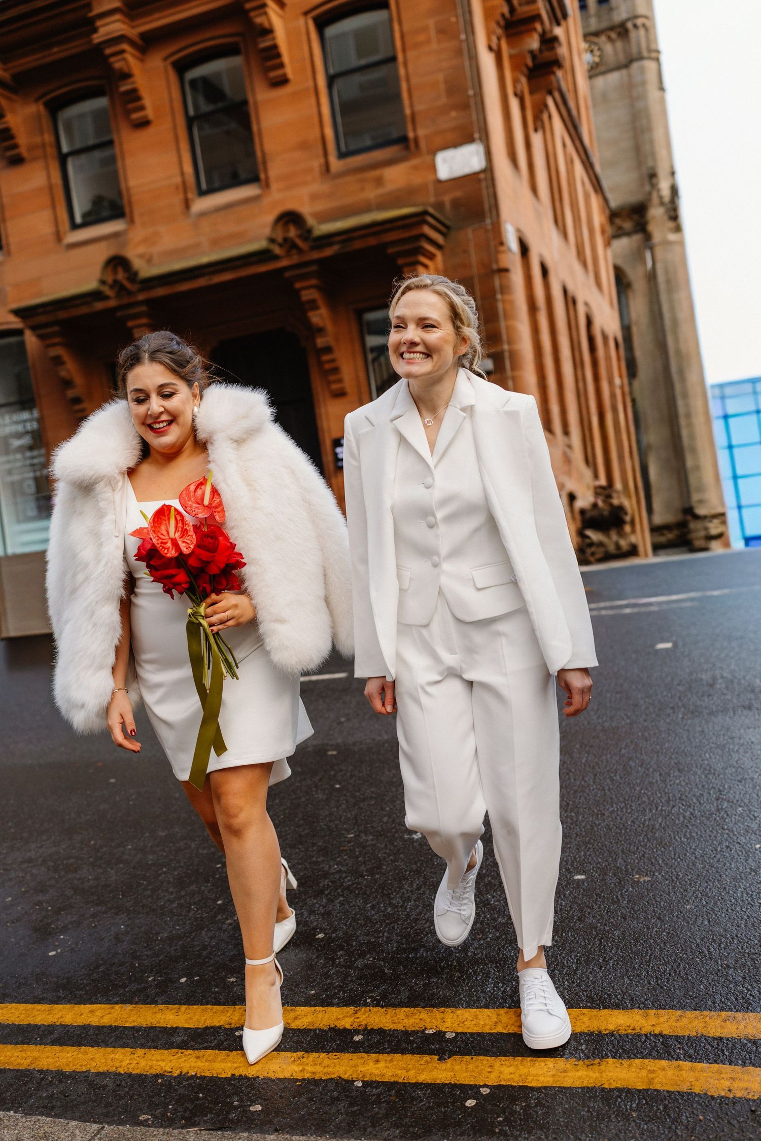 Wedding party walking on a city street wearing all white outfits with red floral accents.