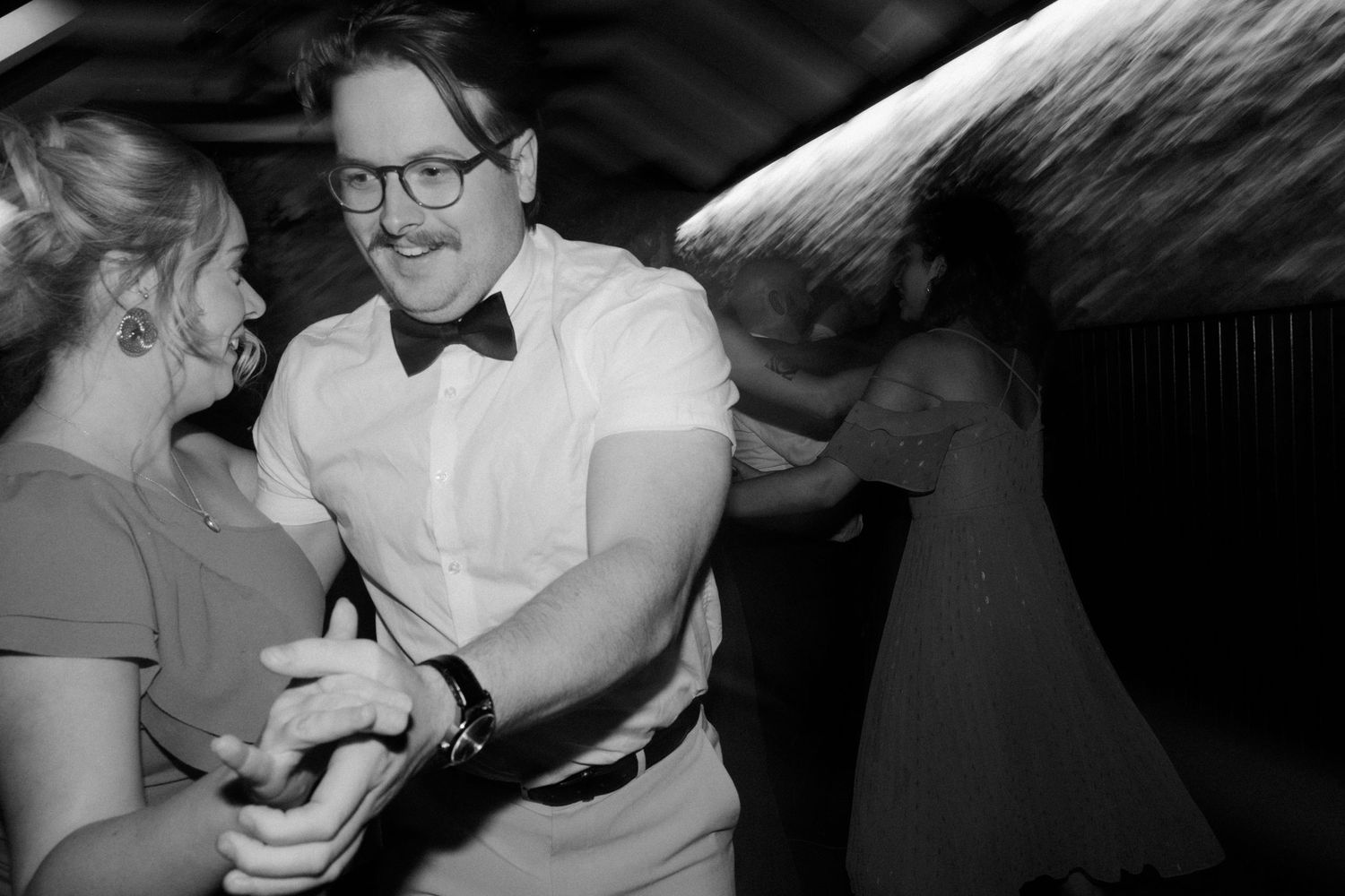 Black and white photo of a couple dancing joyfully at a wedding reception.