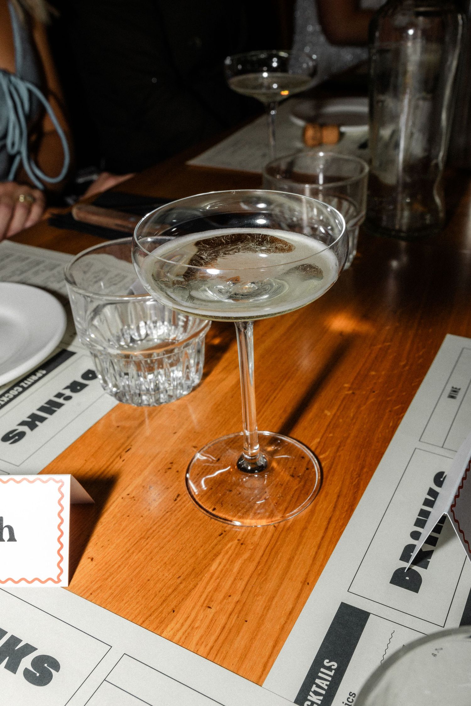 Elegant coupe champagne glass on wooden table beside crystal tumbler at wedding reception drinks setting.