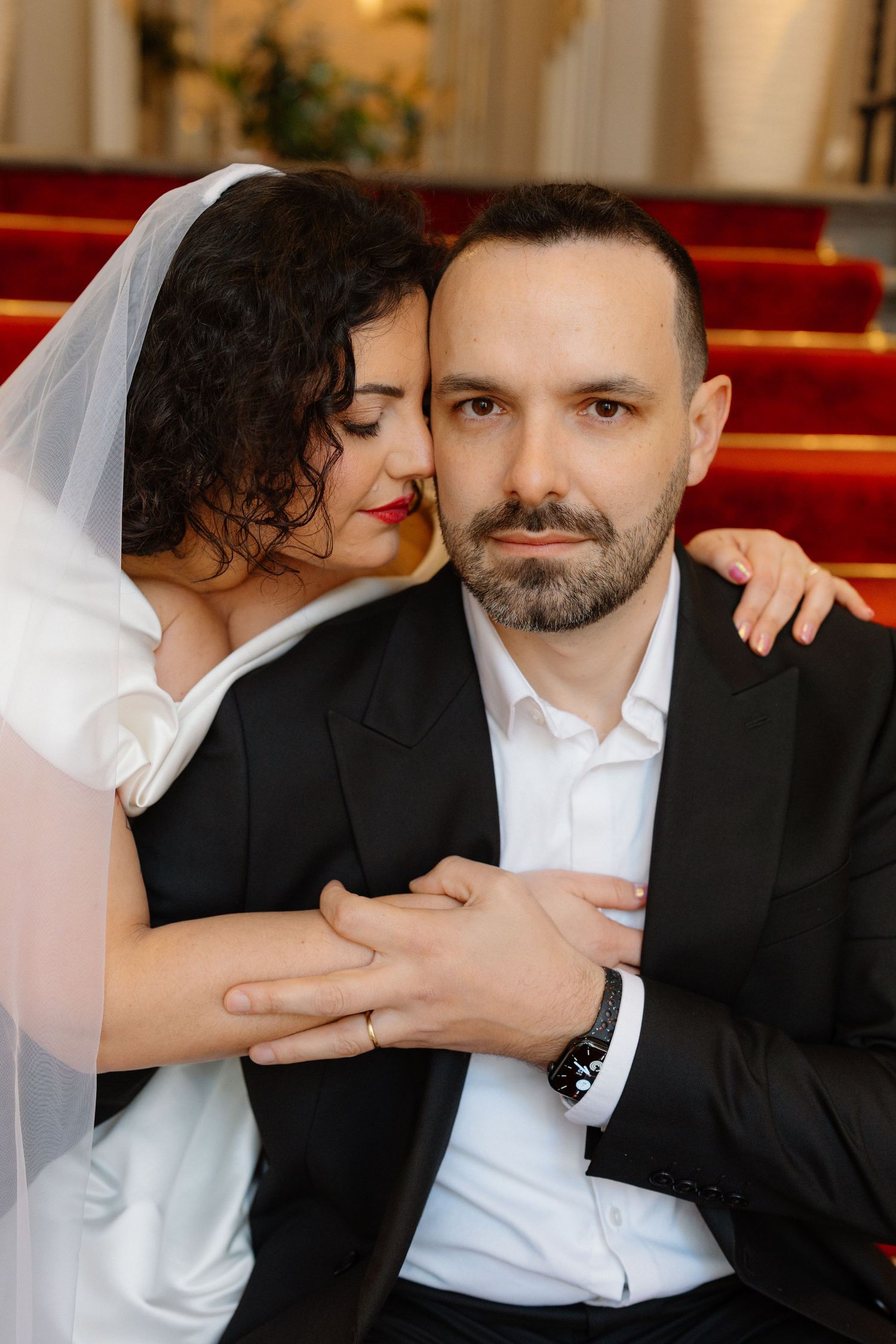 A bride in white veil embraces a bearded groom in black suit during a wedding ceremony in an elegant church.