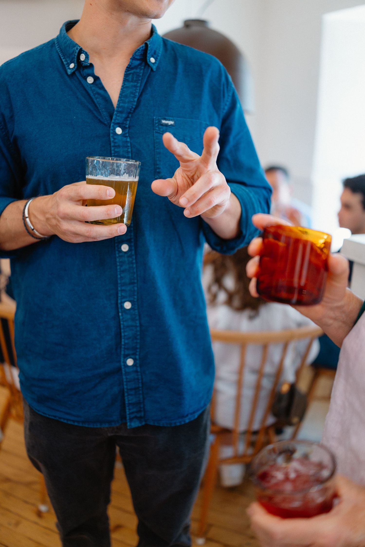 Man in blue denim shirt holding a beer glass gesturing during a wedding reception celebration.