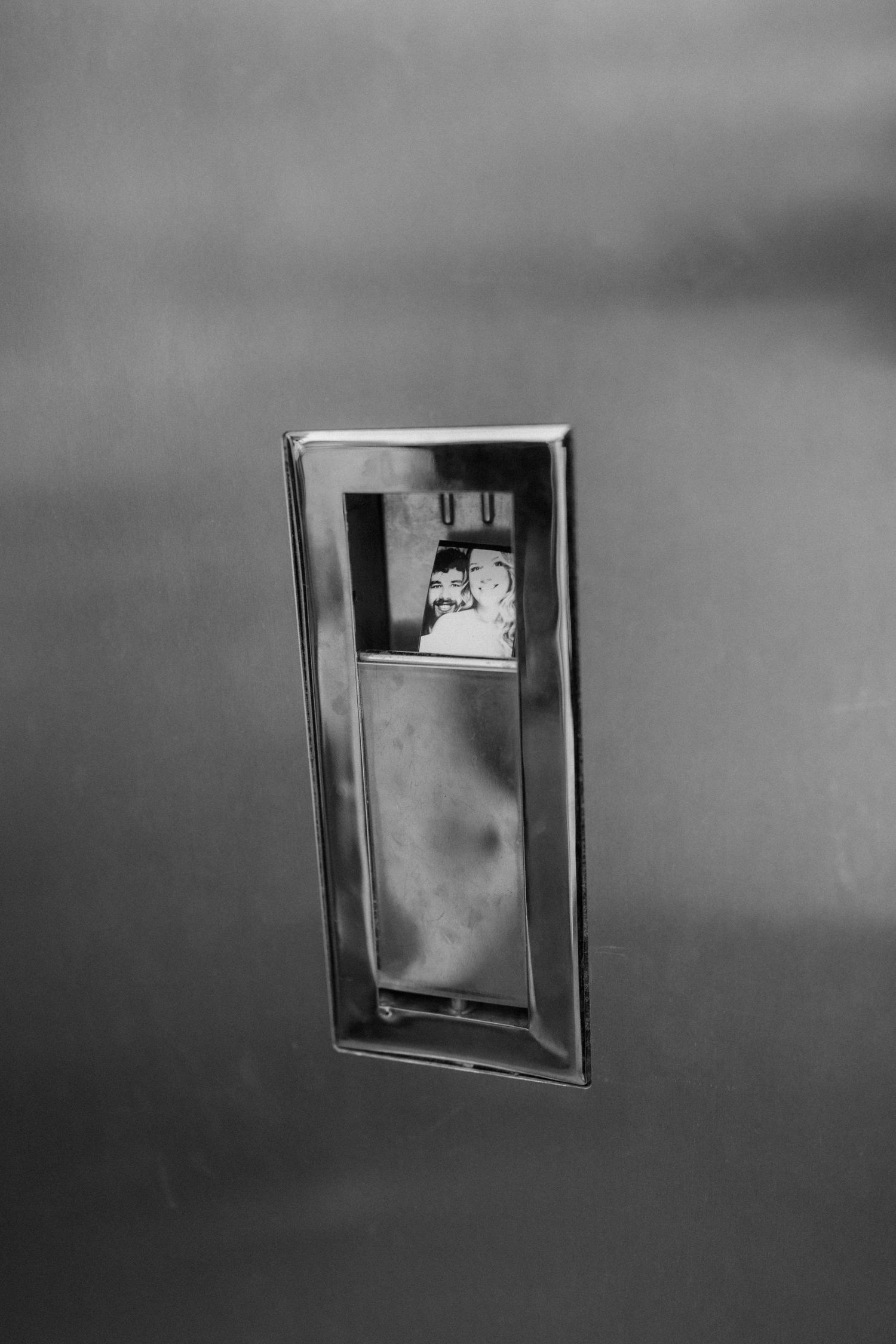 Black and white reflection of bride and groom couple in vintage car chrome door handle.