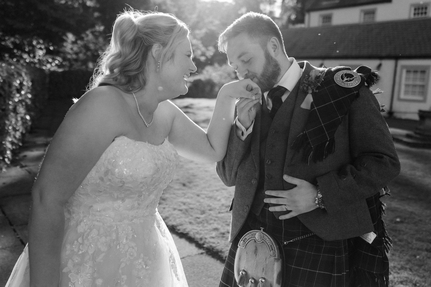 Bride and groom share a tender moment as groom kisses her hand in black and white wedding portrait.