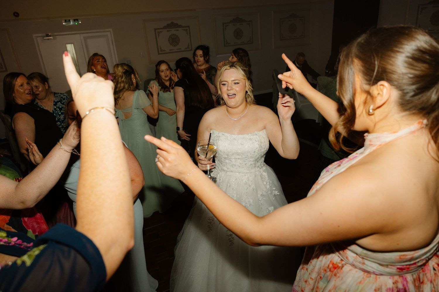 Bride in white gown dancing joyfully with guests at a lively wedding reception party.