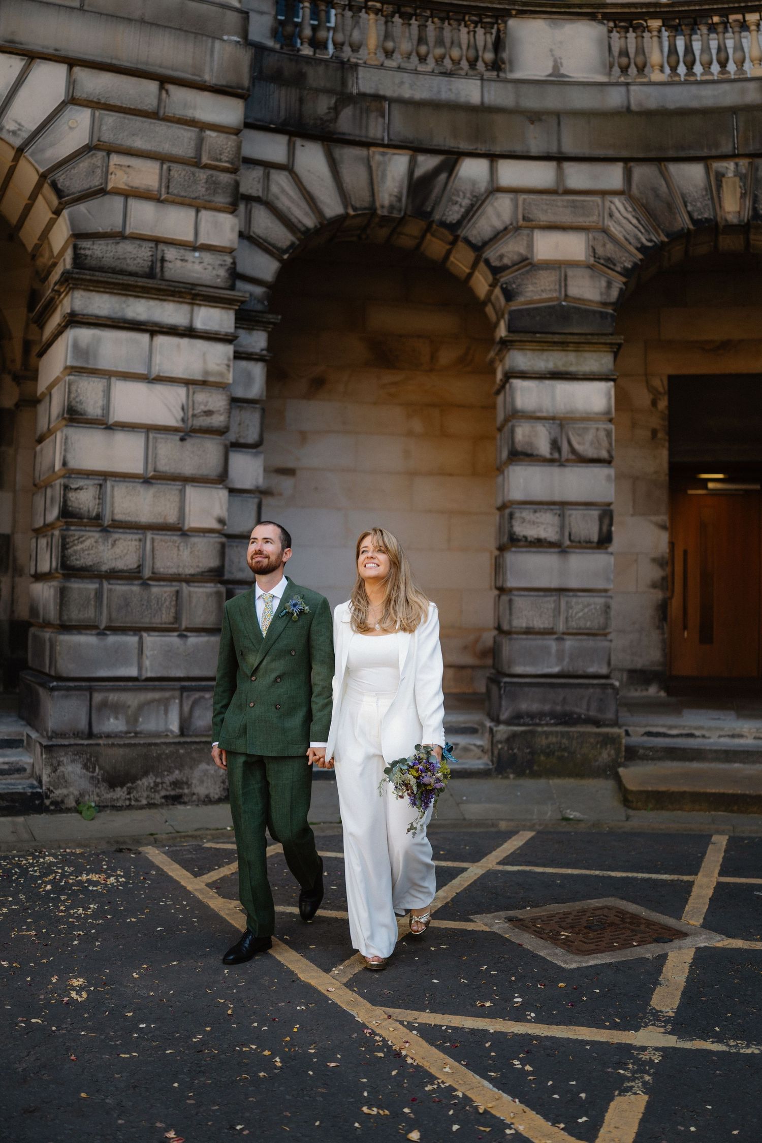 Couple standing beneath stone archways of historic Edinburgh building.