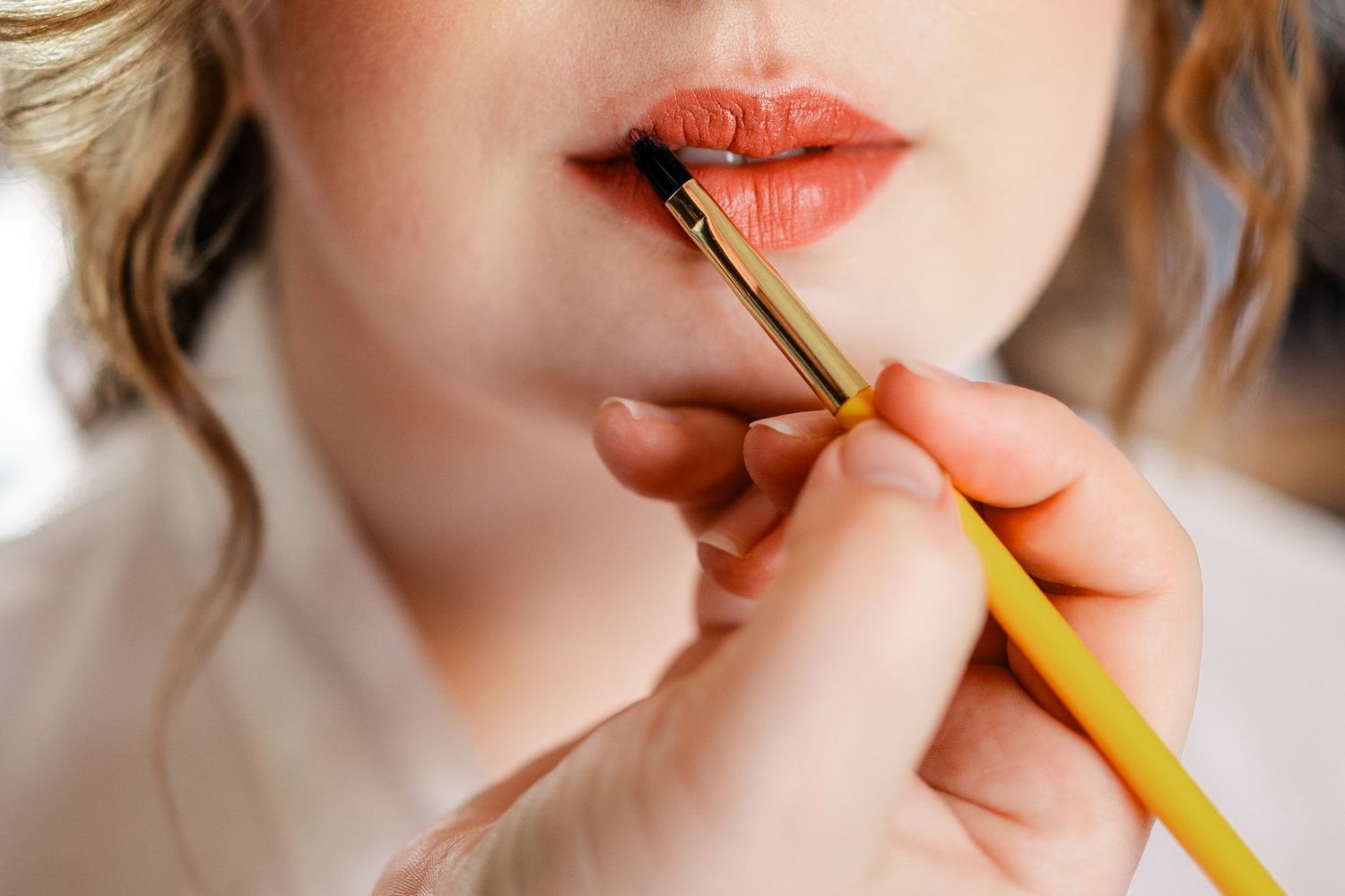 Close-up sequence of someone applying bright red lipstick with a makeup brush.