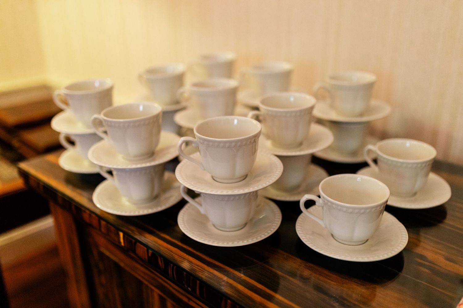 Rows of white teacups and saucers arranged on wooden tables.
