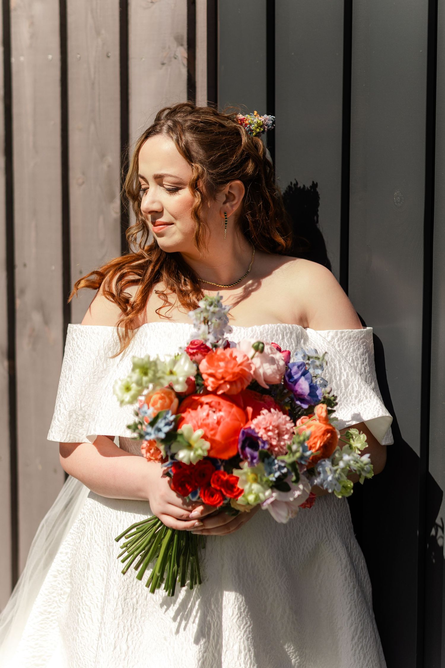 A bridal portrait featuring an off-shoulder white gown and vibrant coral and purple bouquet.
