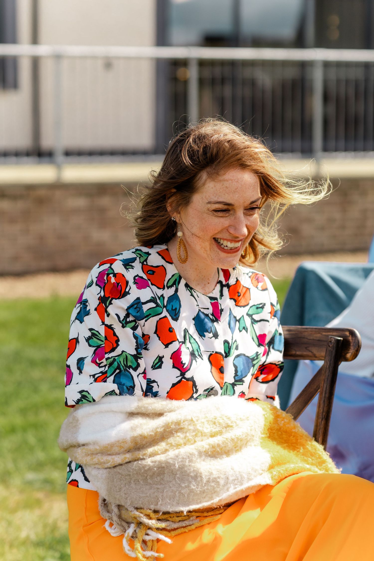 A person in a floral print shirt laughing while enjoying a sunny outdoor gathering.