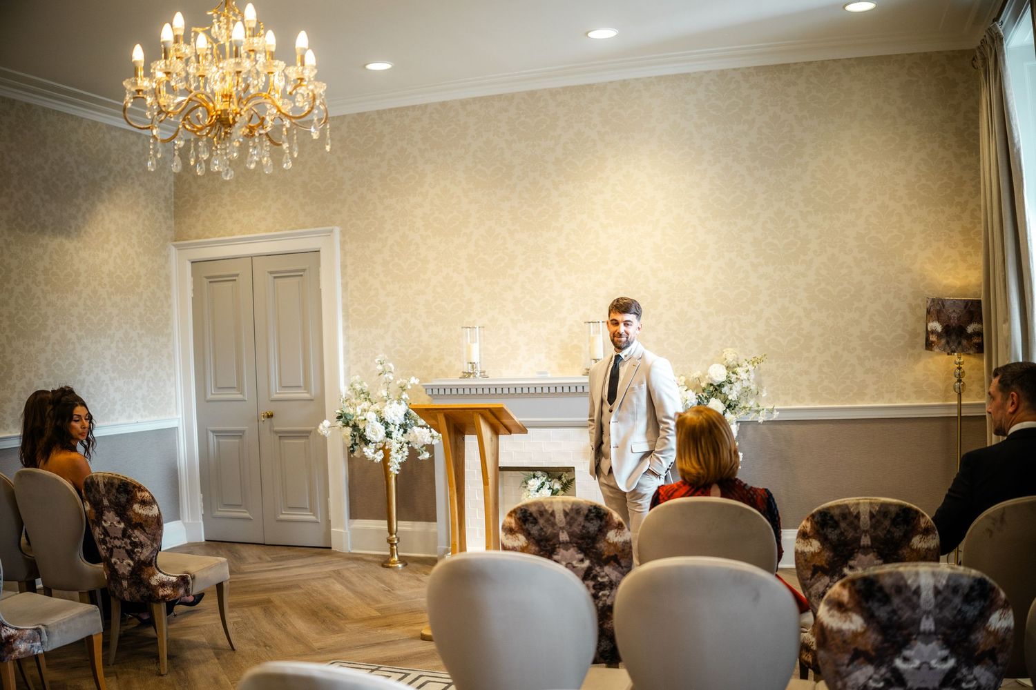 Elegant reception room with crystal chandelier and white chairs set for wedding ceremony.