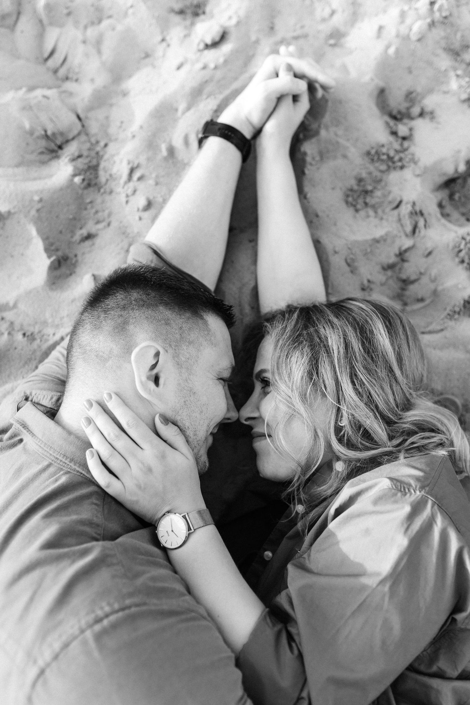 Intimate black and white portrait of couple lying on sandy beach.