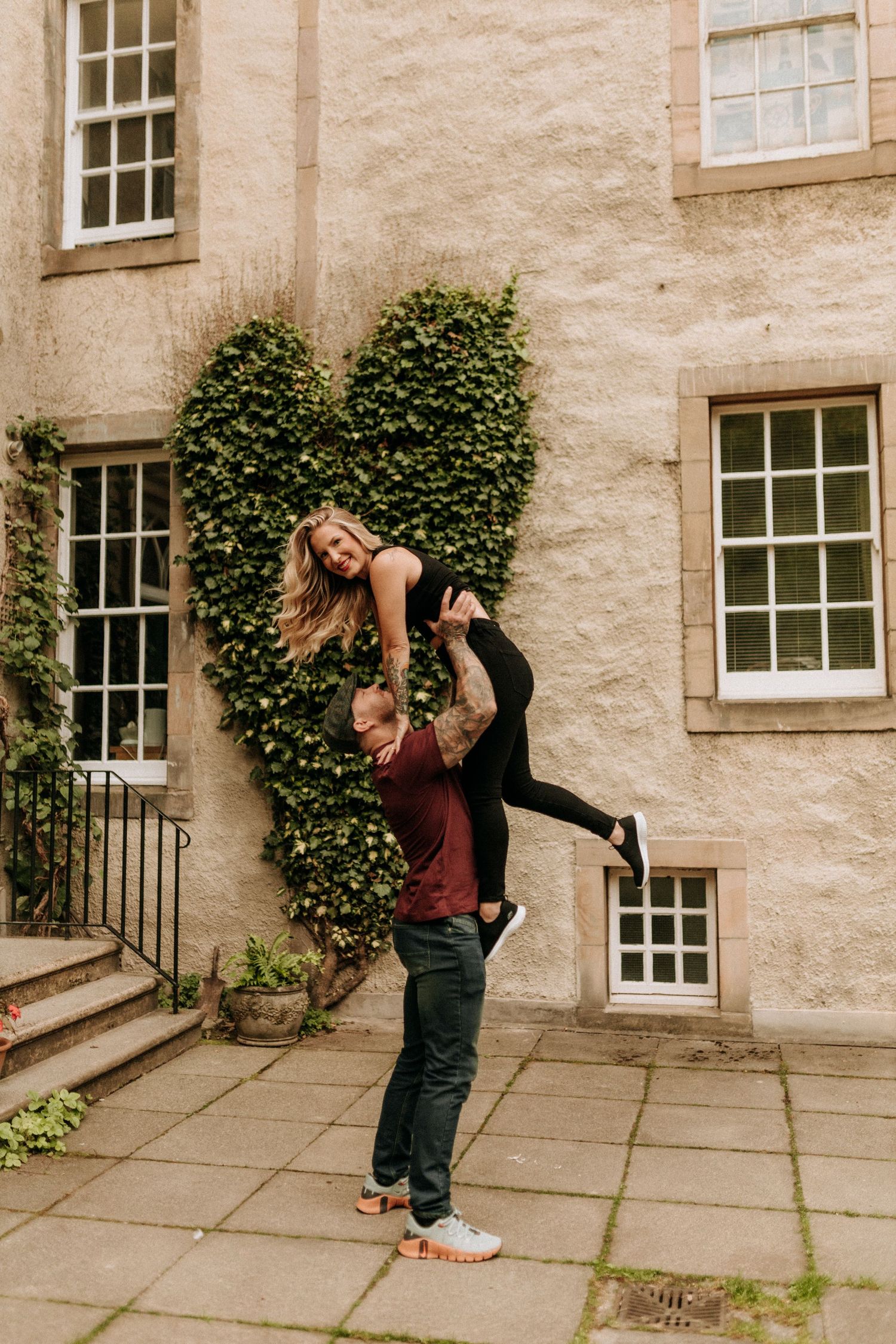 Dancing couple performing romantic dips against stone building with ivy and windows.