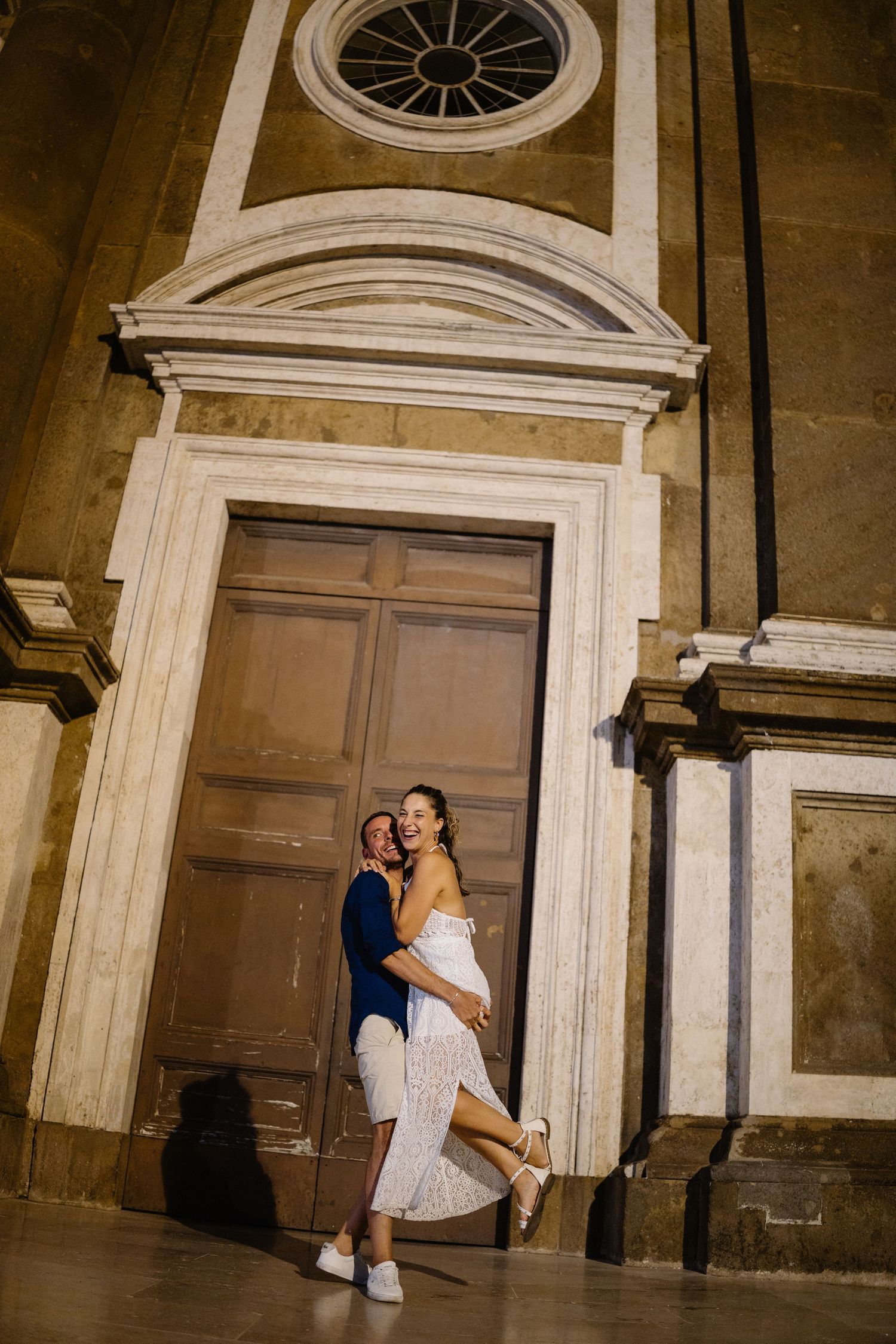 Couple embracing by historic wooden doors and stone archways of classic building.