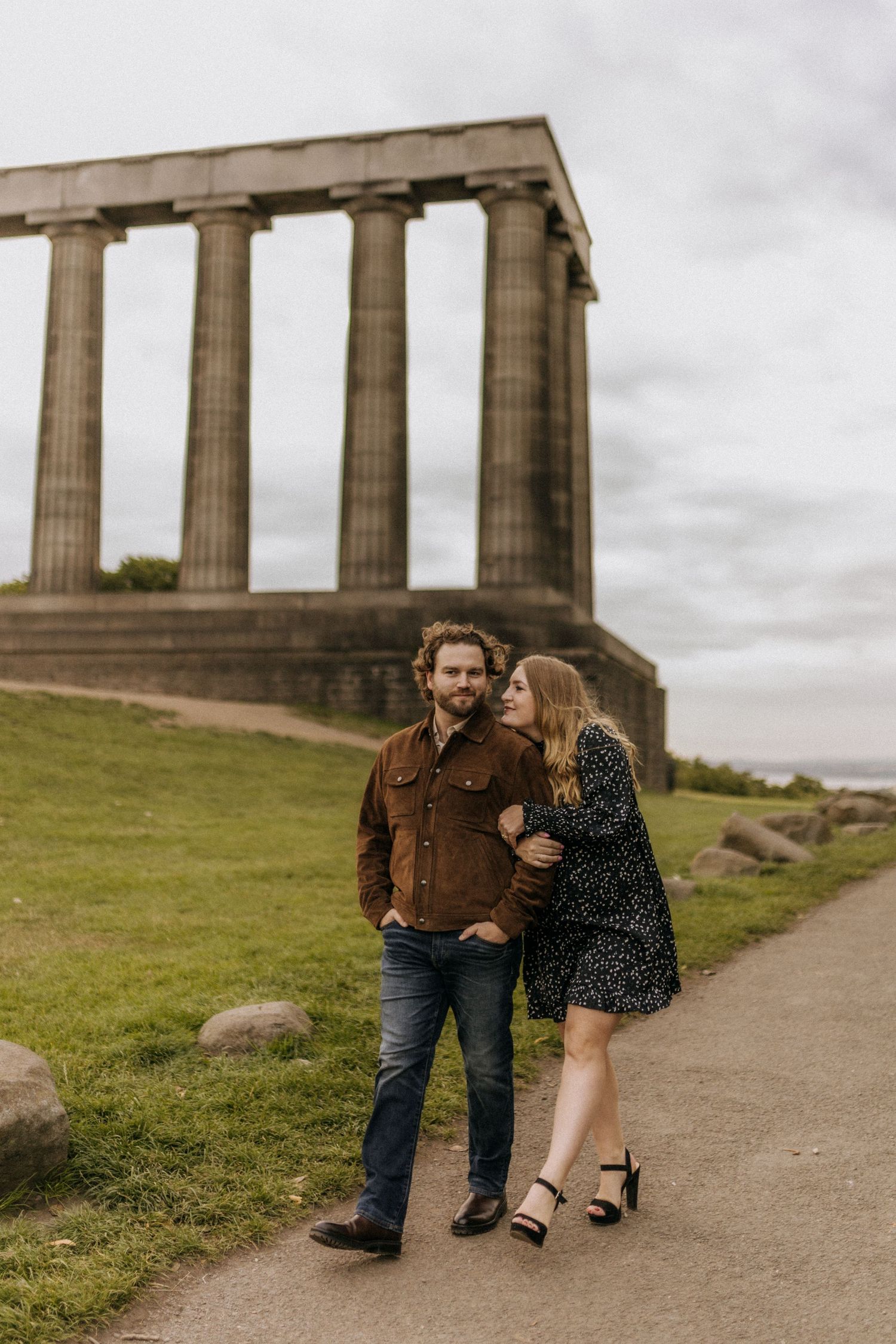 A couple poses together near ancient Greek-style stone columns on a cloudy day.